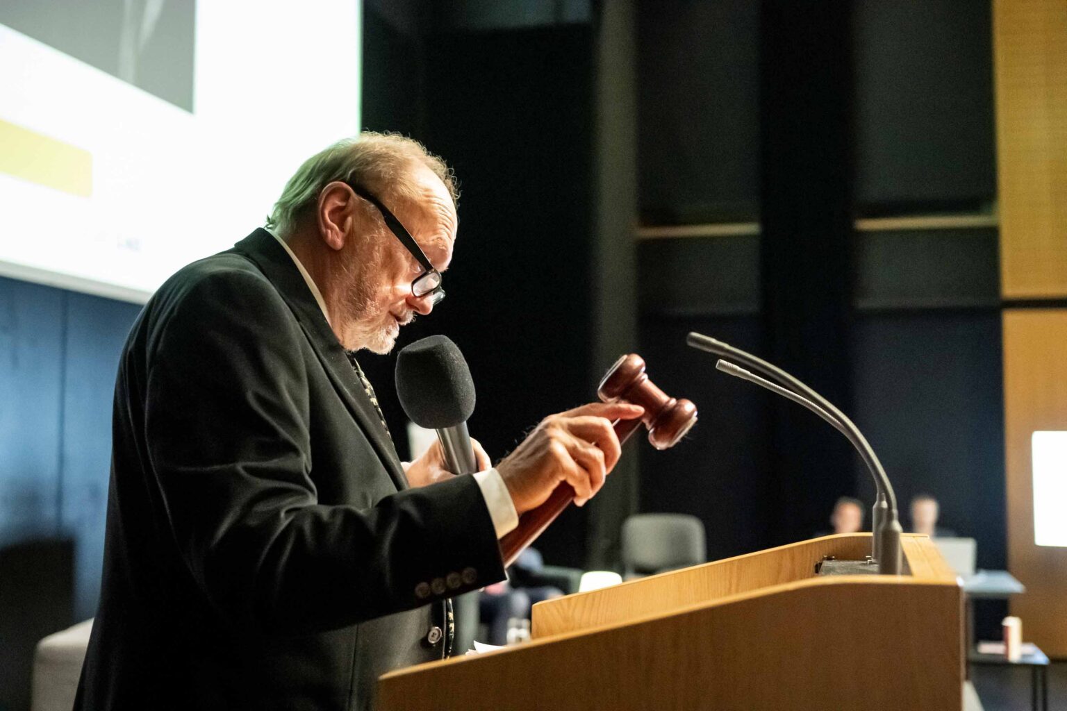 Mężczyzna w garniturze na mównicy, w ręku trzyma aukcyjny młotek