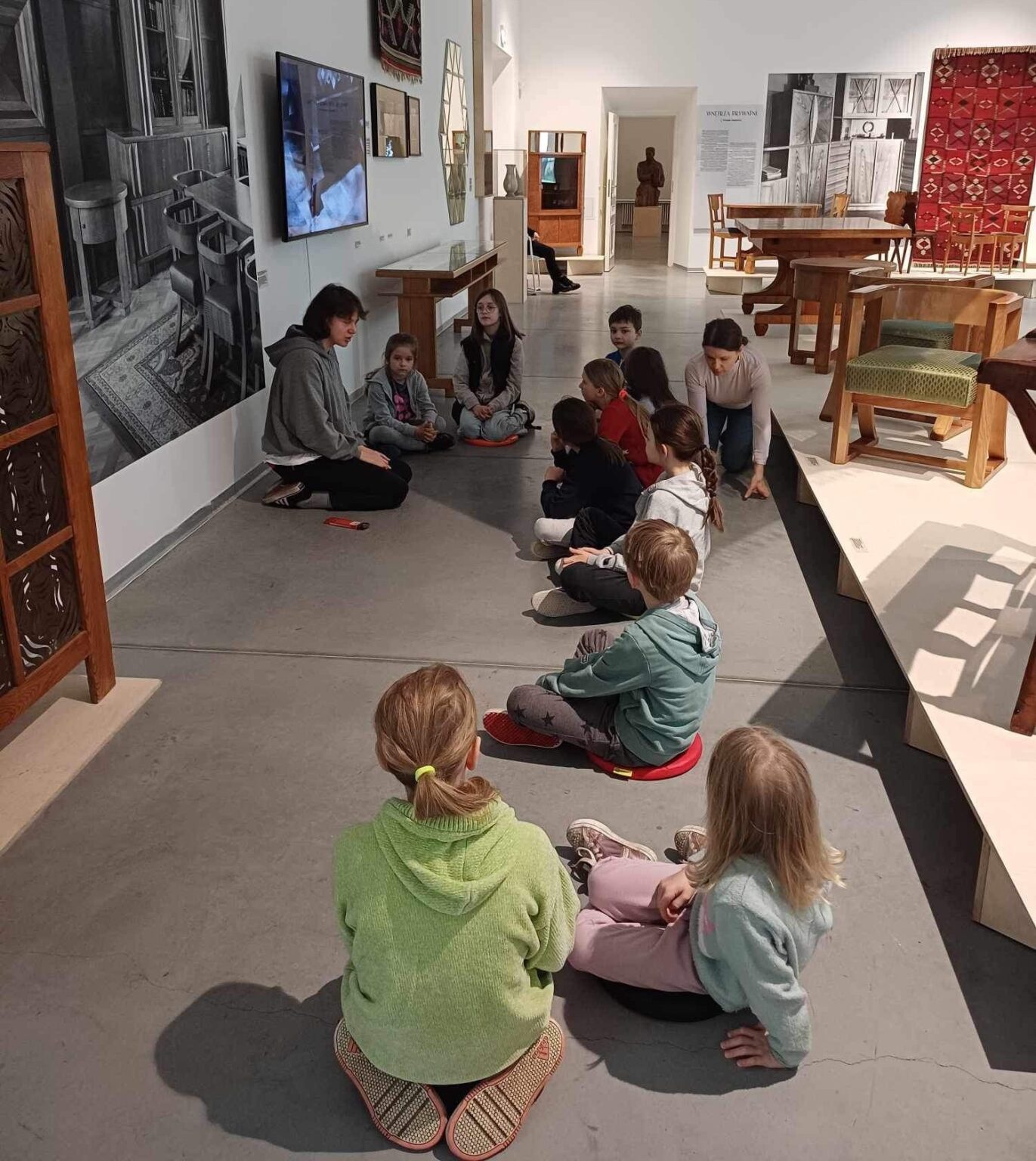 grupa dzieci siedzi na podłodze w przestrzeni wystawy