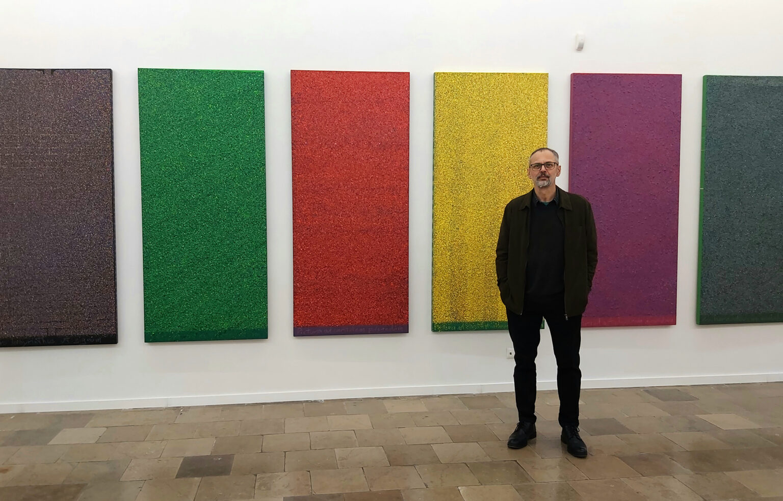 mężczyzna stoi na tle dużych, pionowych , kolorowych obrazów