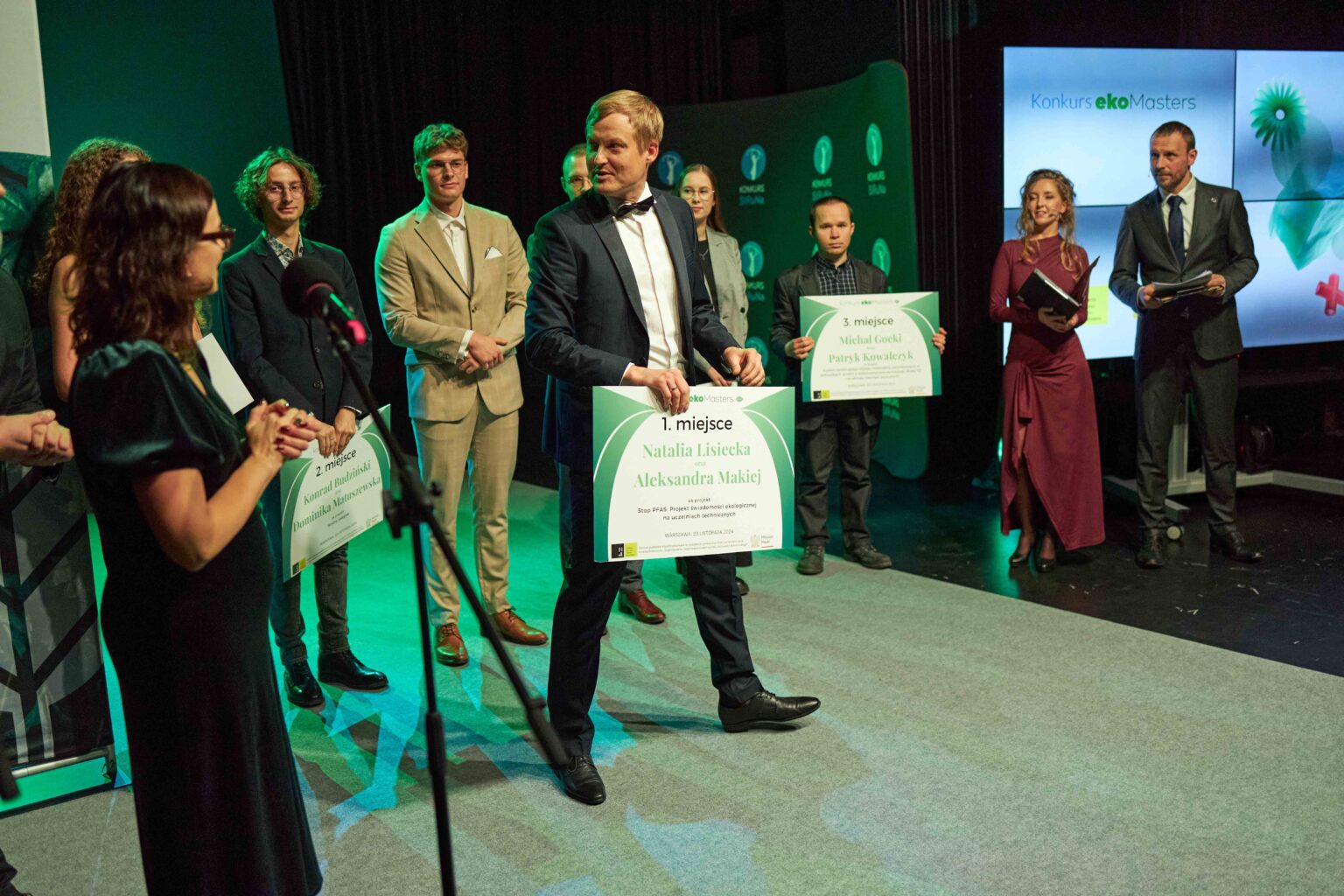 mężczyzna w garniturze z dyplomem na scenie