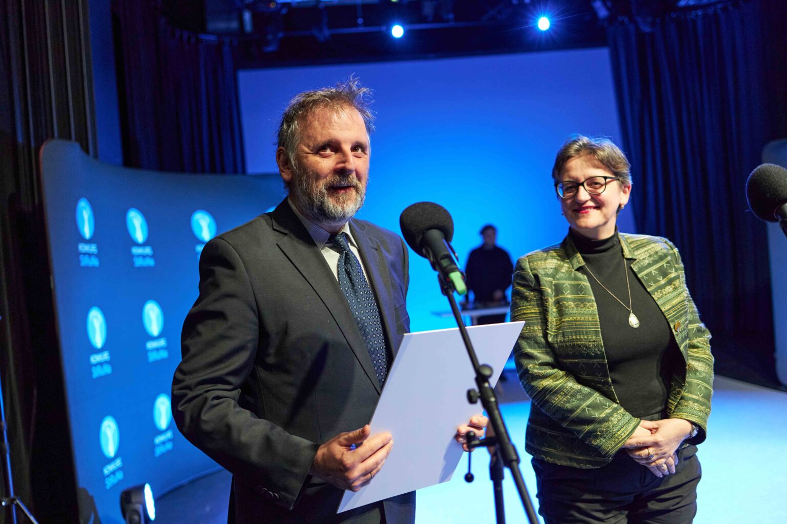 mężczyzna przy mikrofonie z kartką w dłoniach