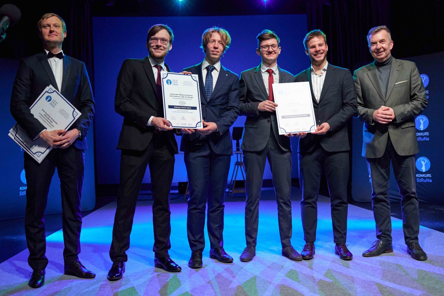 czterech mężczyzn w garniturach pozuje z dyplomami