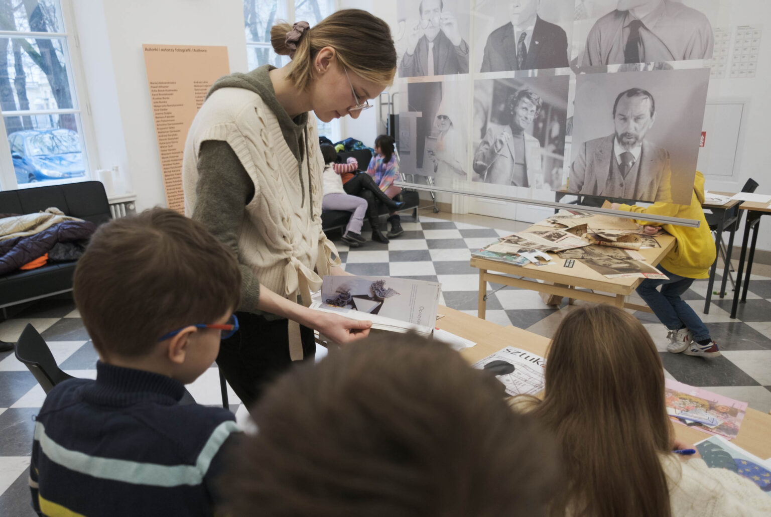 młoda kobieta otoczona dziećmi przy stole z gazetamiie
