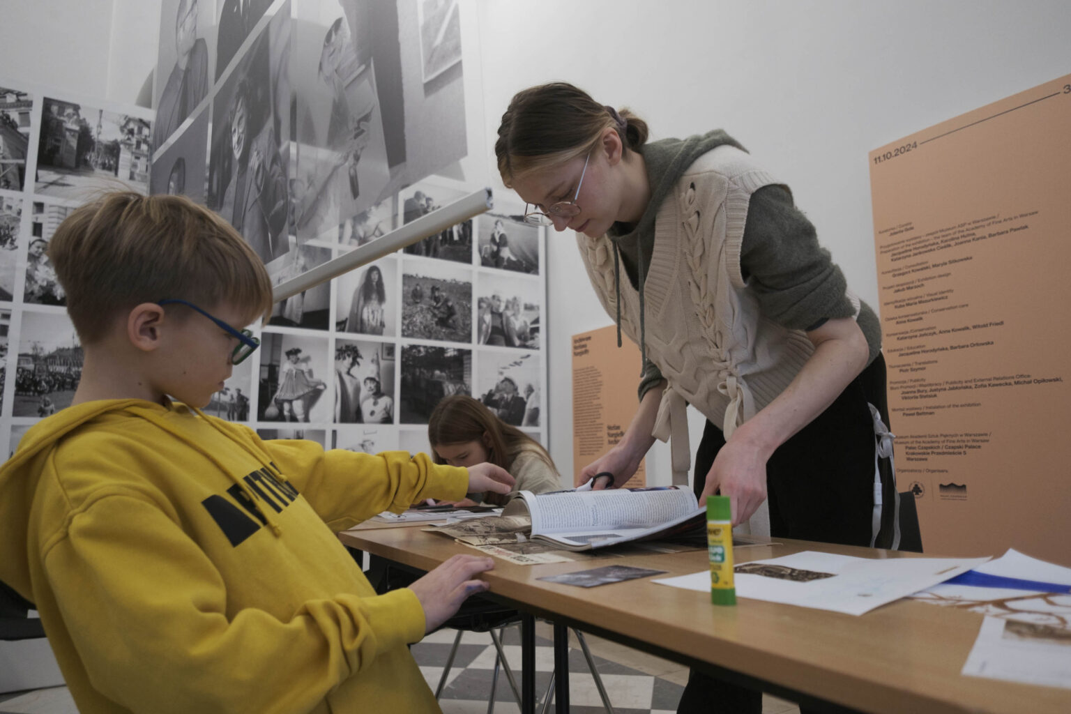 chłopiec w żółtej bluzie i młoda kobieta przy stole z gazetami i materiałami plastycznymi