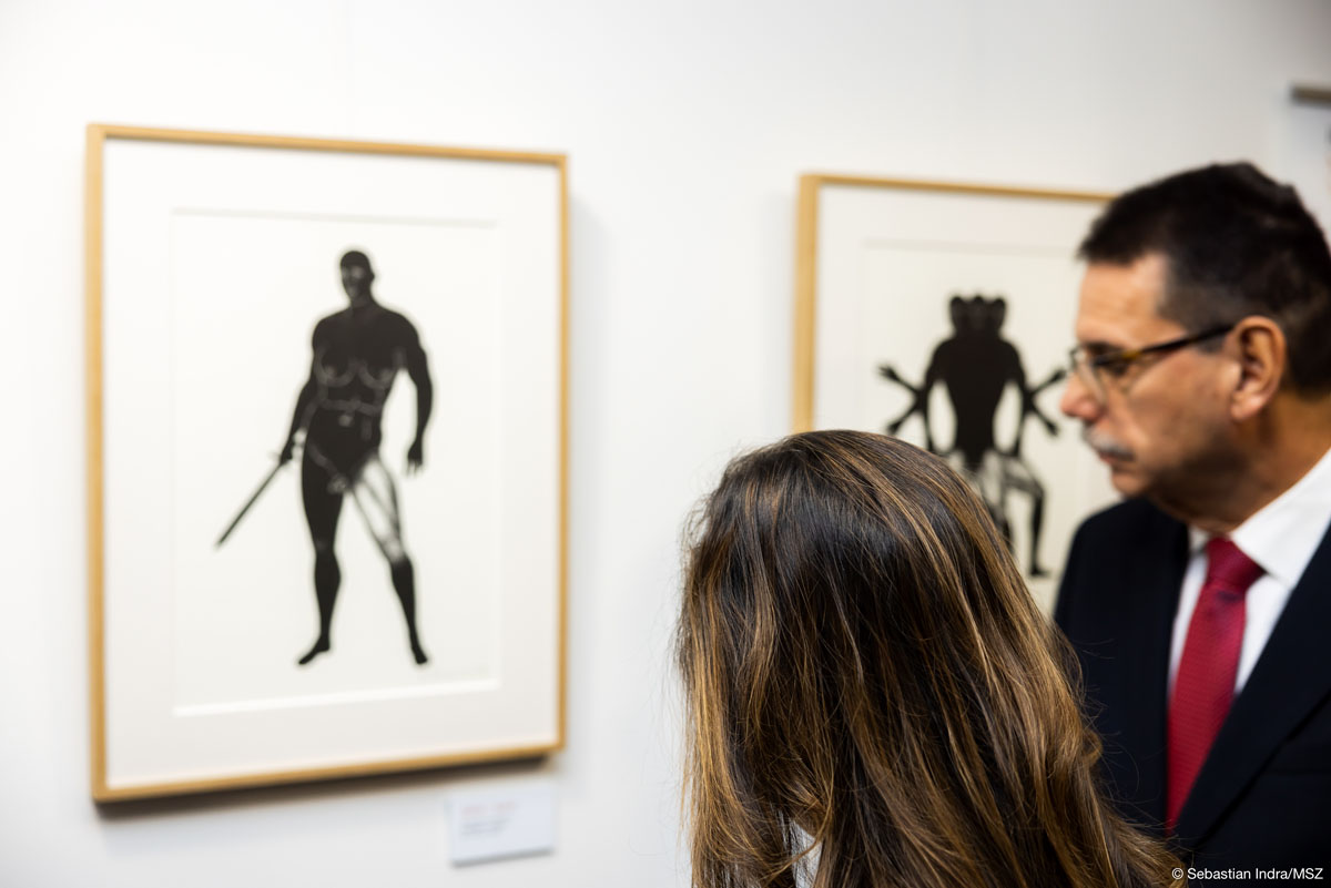 Kobieta i mężczyzna patrzą na eksponowane na białej ścianie czarno-białe grafiki.