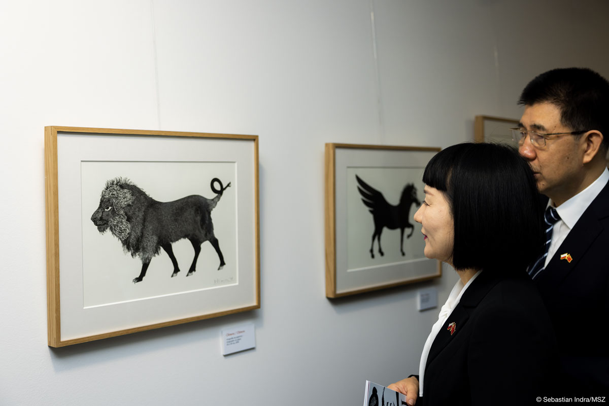 Kobieta i mężczyzna patrzą na eksponowane na białej ścianie czarno-białe grafiki.