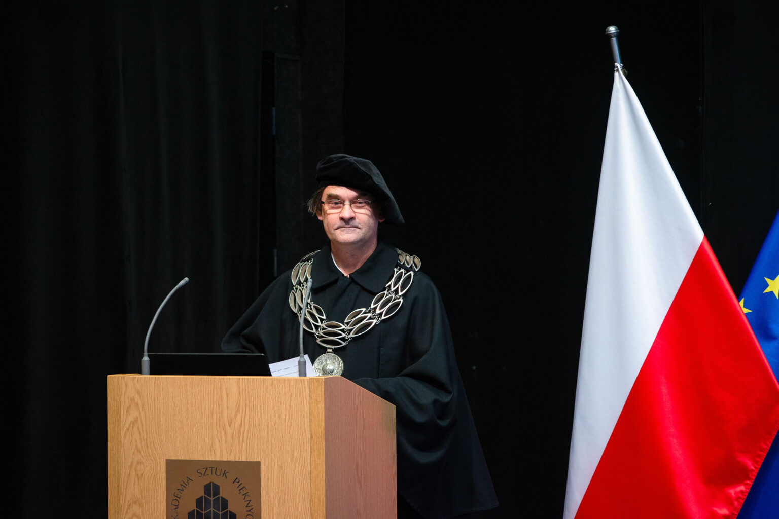 mężczyzna w stroju reprezentacyjnym uczelni wyższej przy mikrofonie