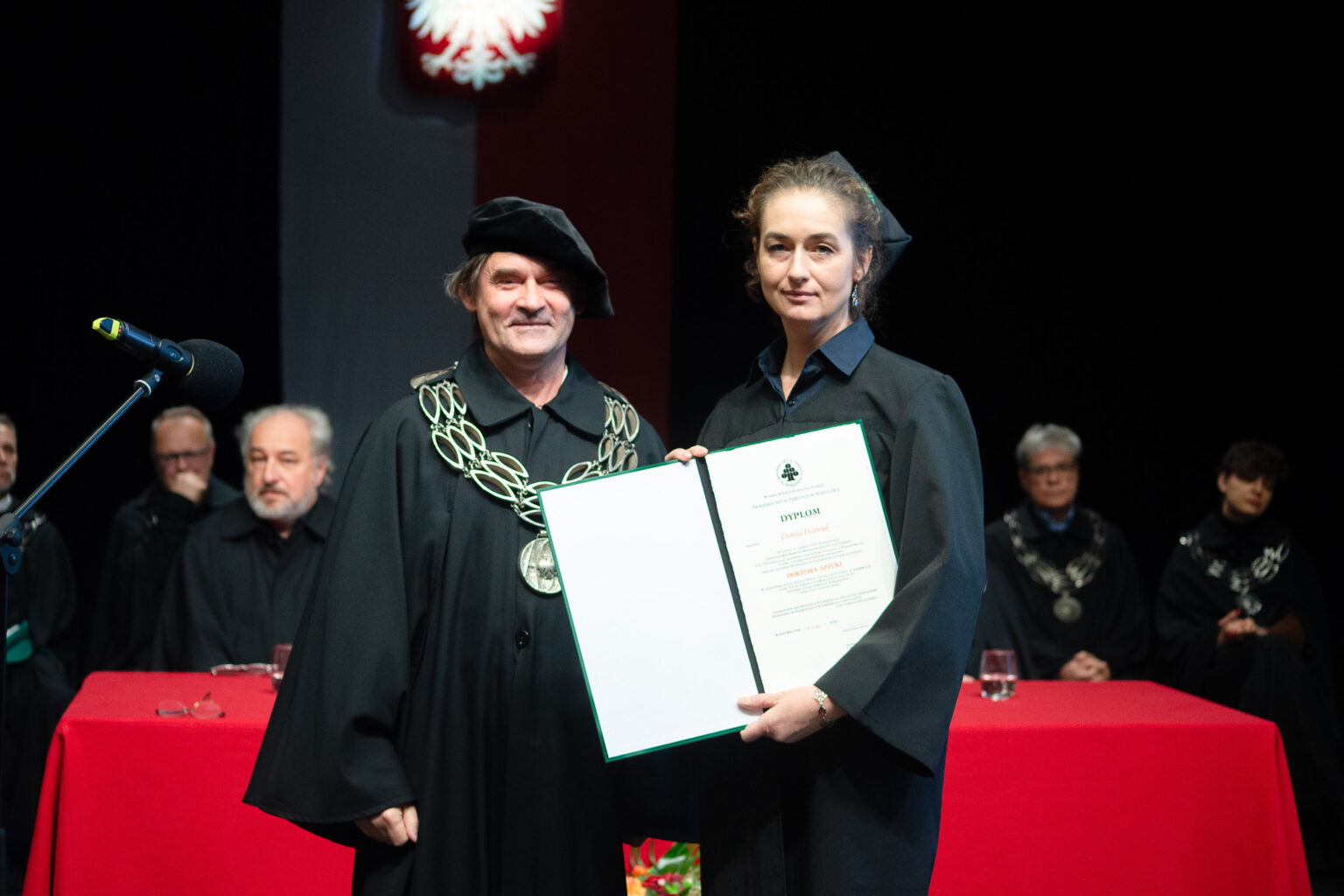 mężczyzna i kobieta w strojach reprezentacyjnym ASP w Warszawie, kobieta z dyplomem