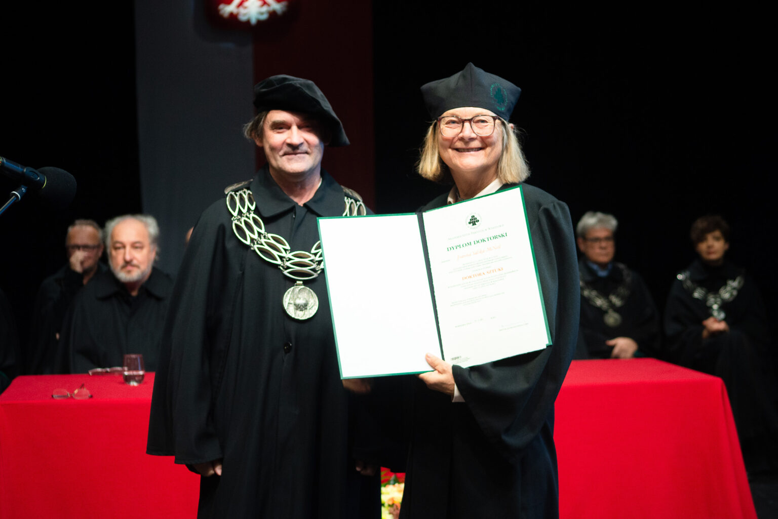 mężczyzna i kobieta w strojach reprezentacyjnym ASP w Warszawie, kobieta z dyplomem