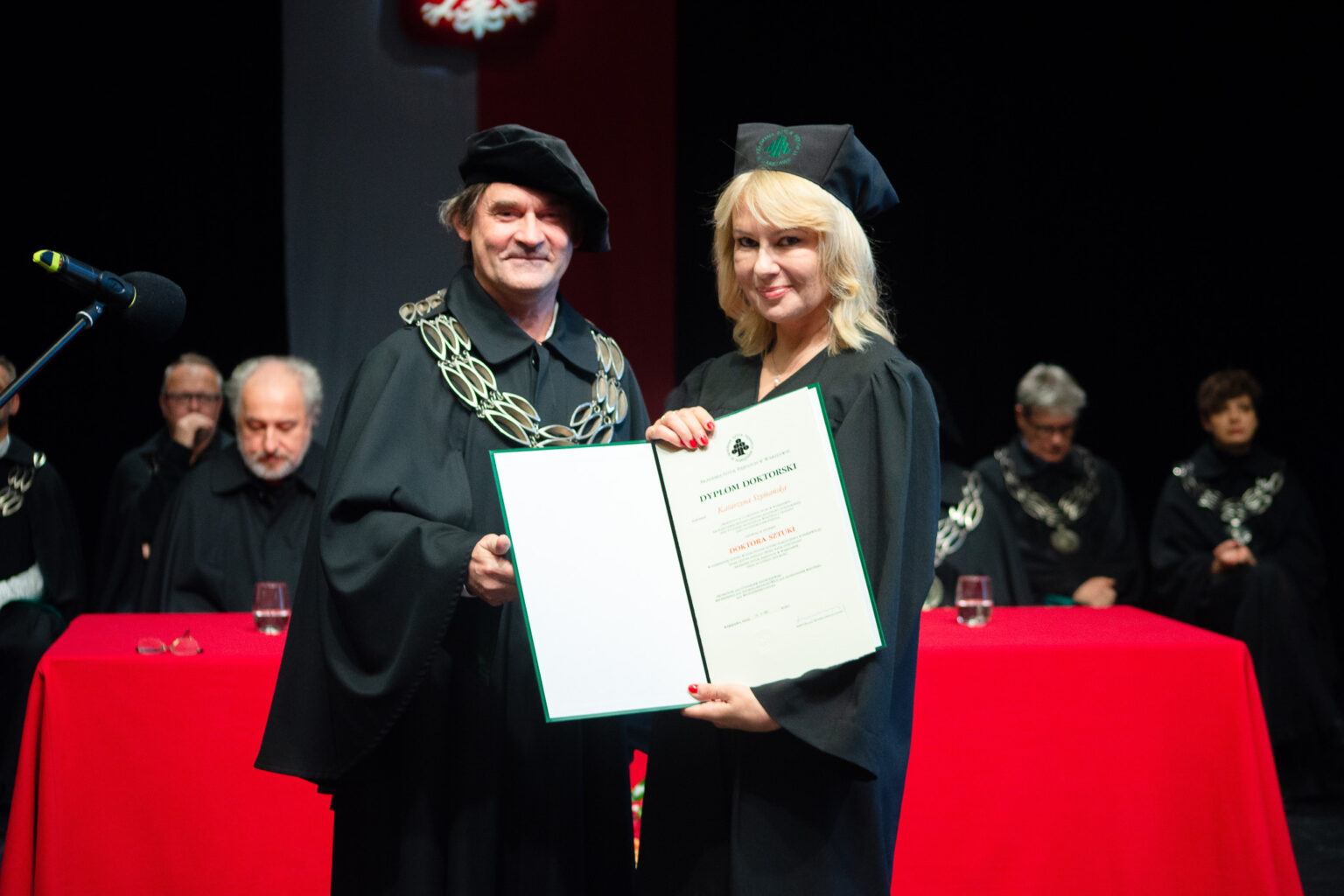 mężczyzna i kobieta w strojach reprezentacyjnym ASP w Warszawie, kobieta z dyplomem