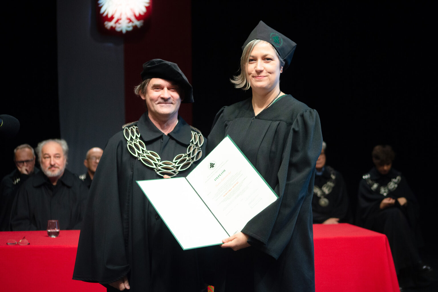 mężczyzna i kobieta w strojach reprezentacyjnym ASP w Warszawie, kobieta z dyplomem