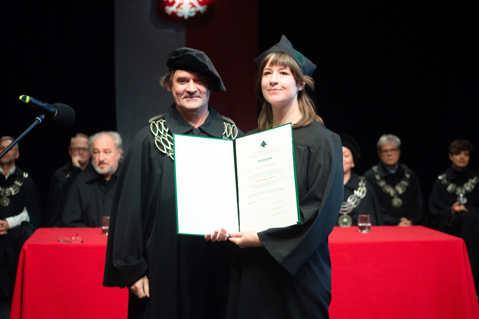 mężczyzna i kobieta w strojach reprezentacyjnym ASP w Warszawie, kobieta z dyplomem