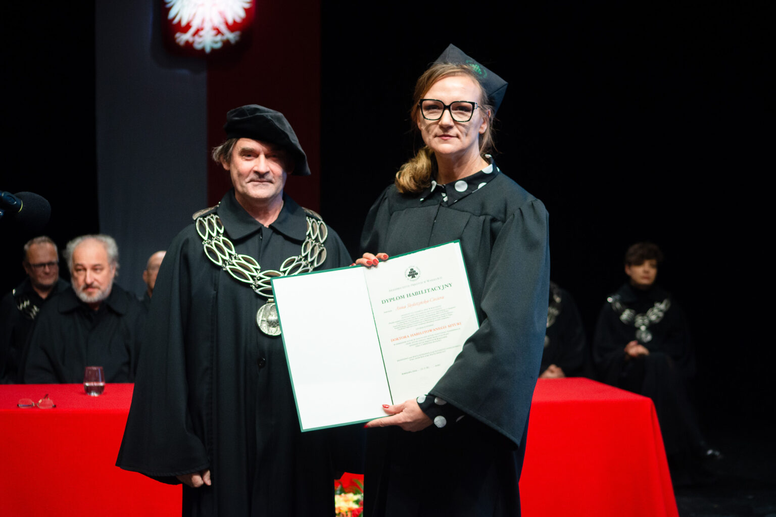 mężczyzna i kobieta w strojach reprezentacyjnym ASP w Warszawie, kobieta z dyplomem