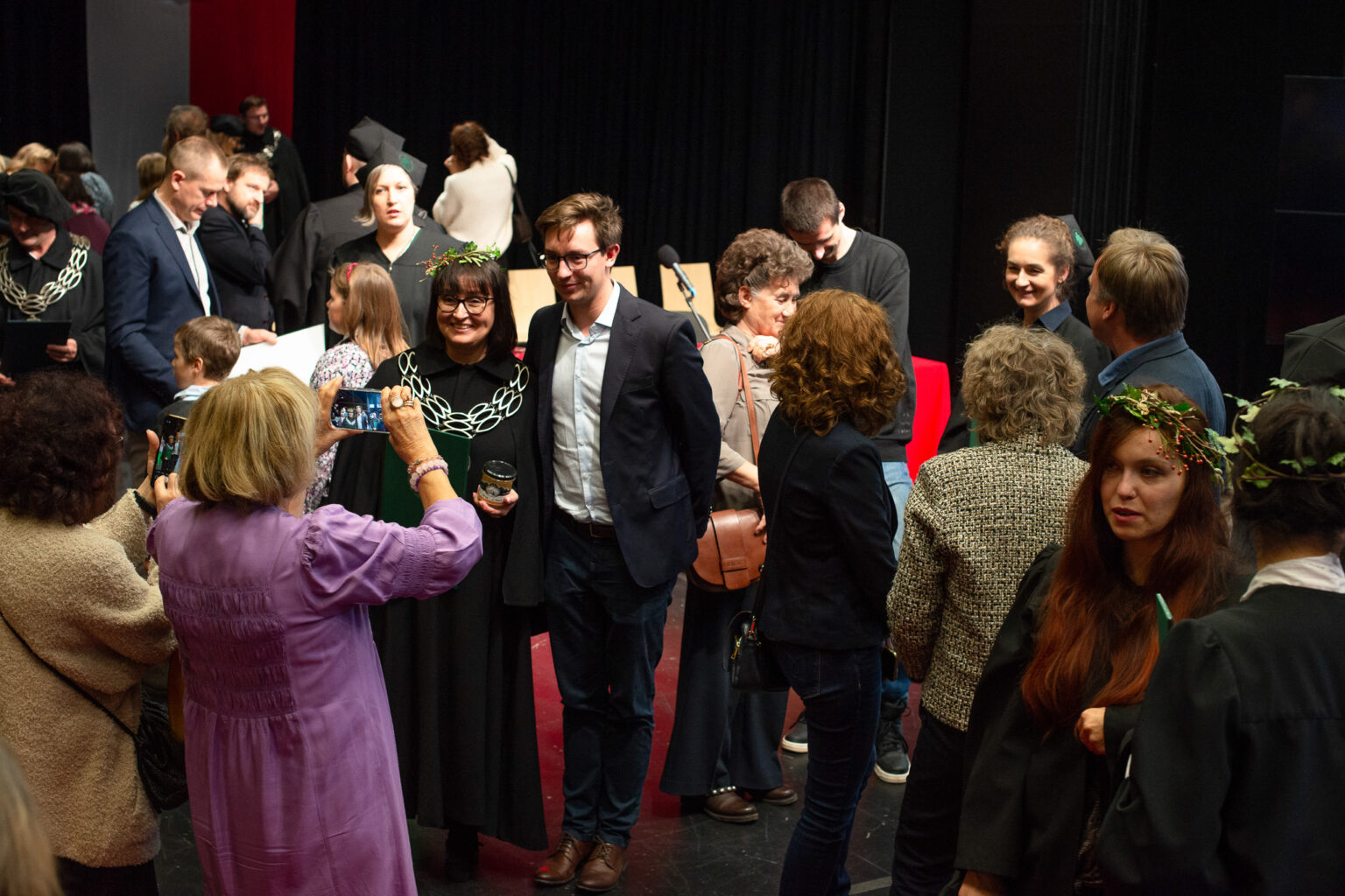 osoby pozują do zdjęcia kobiecie w filetowej sukience z telefonem