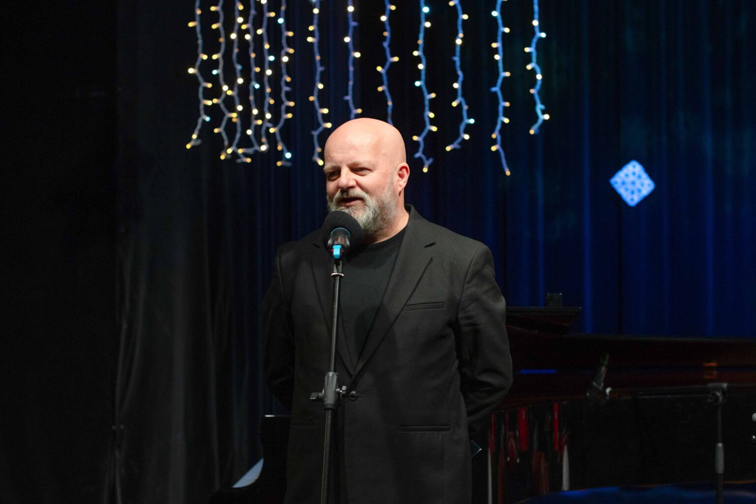 mężczyzna przy mikrofonie, lampki świąteczne w tle