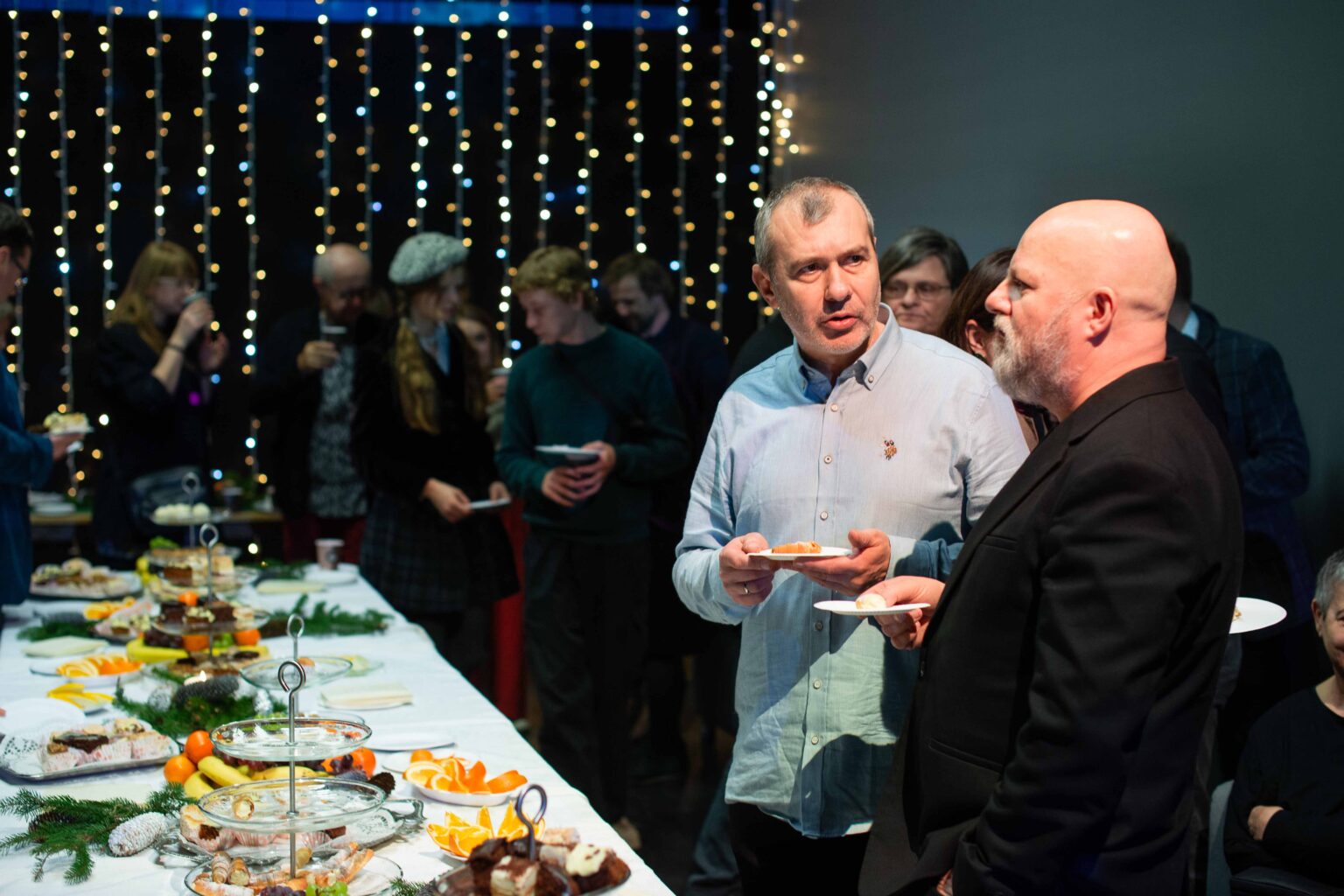 dwaj mężczyźni rozmawiają, obok świąteczny stół, lampki w tle