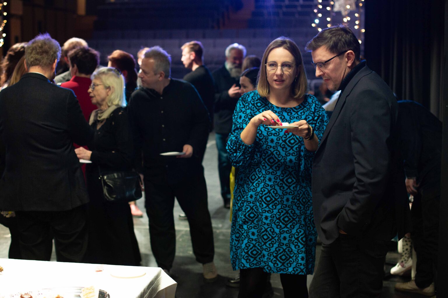 grupa ludzi rozmawiających, obok stół z białym obrusem