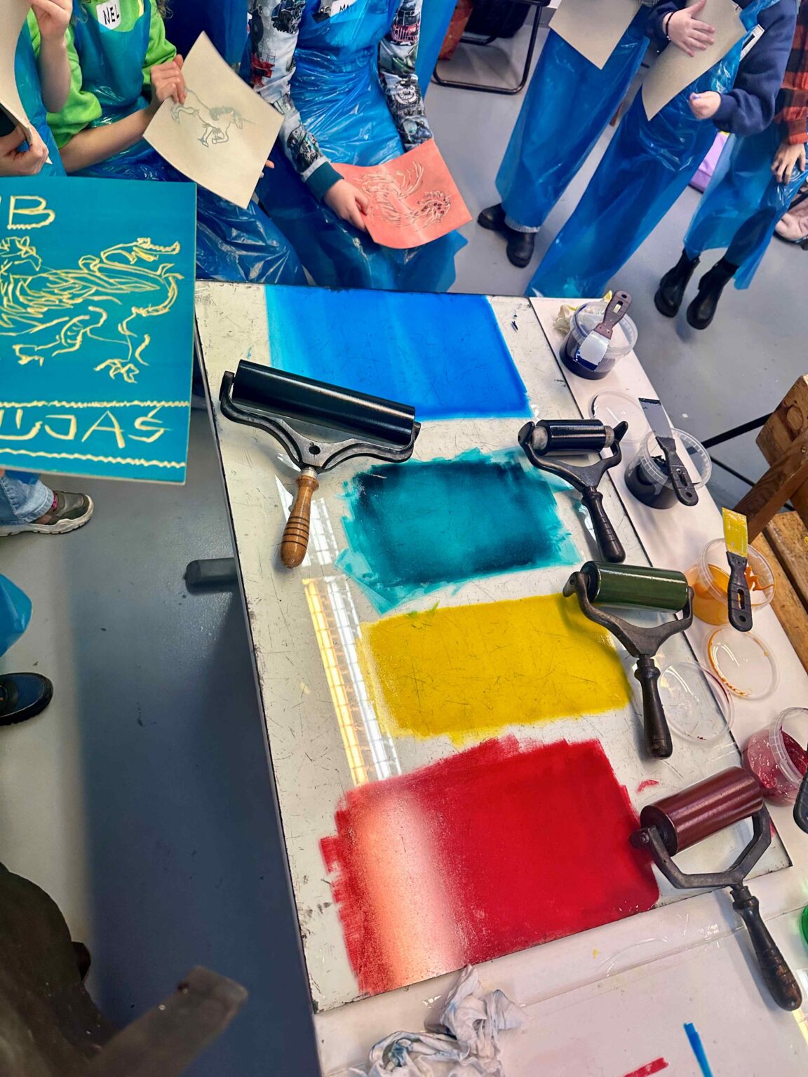 Grupa dzieci przy dużym stole podczas warsztatów. Na stole przybory do rysowania