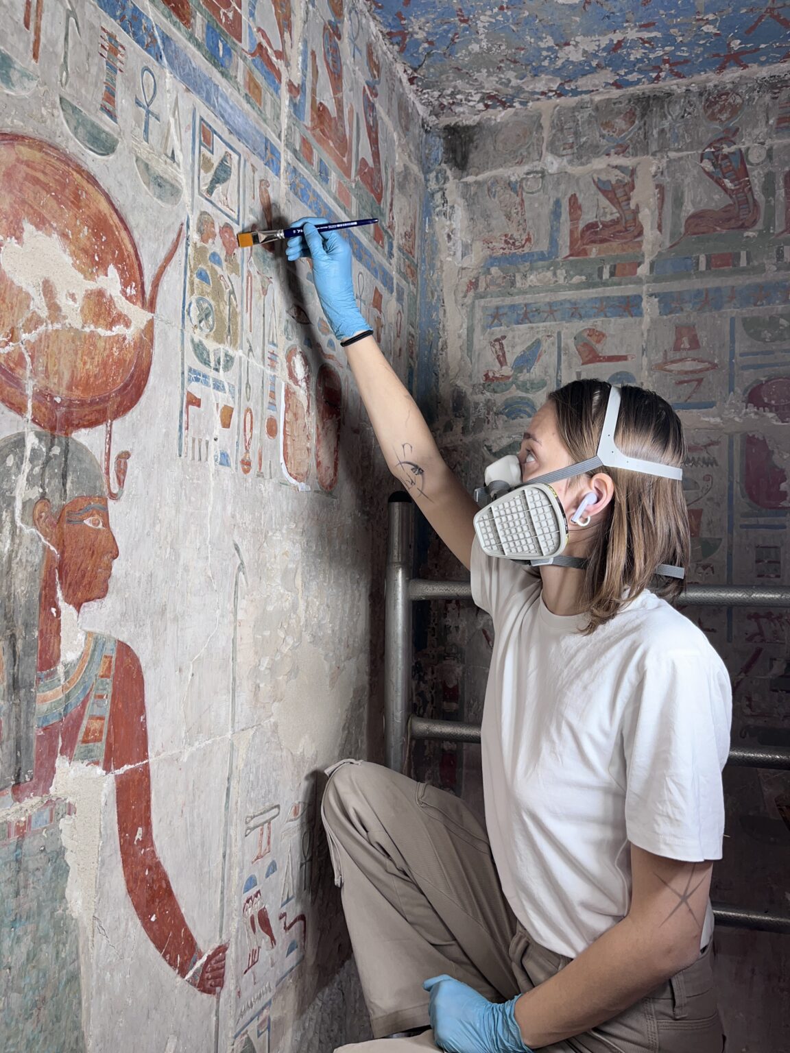 Dziewczyna w masce i rękawiczkach, z pędzlem w ręku wykonuje prace konserwatorskie w świątyni