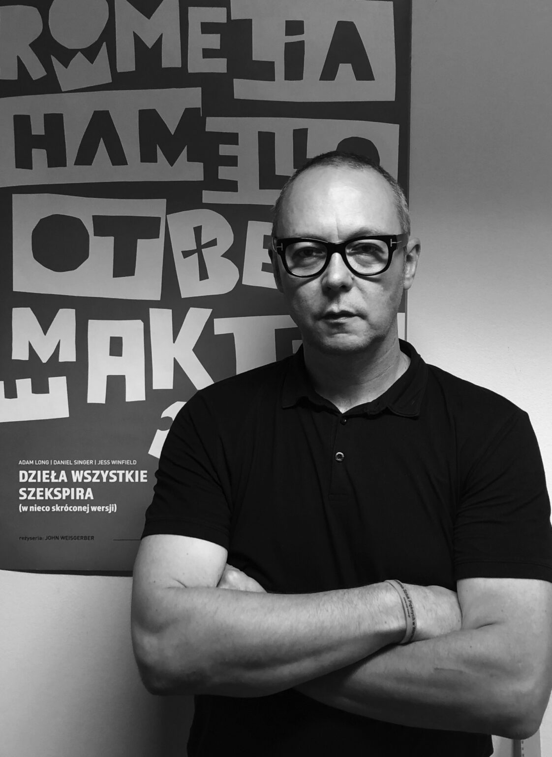 czarno-biały portret mężczyzny w okularach z założonymi rękoma, plakat w tle