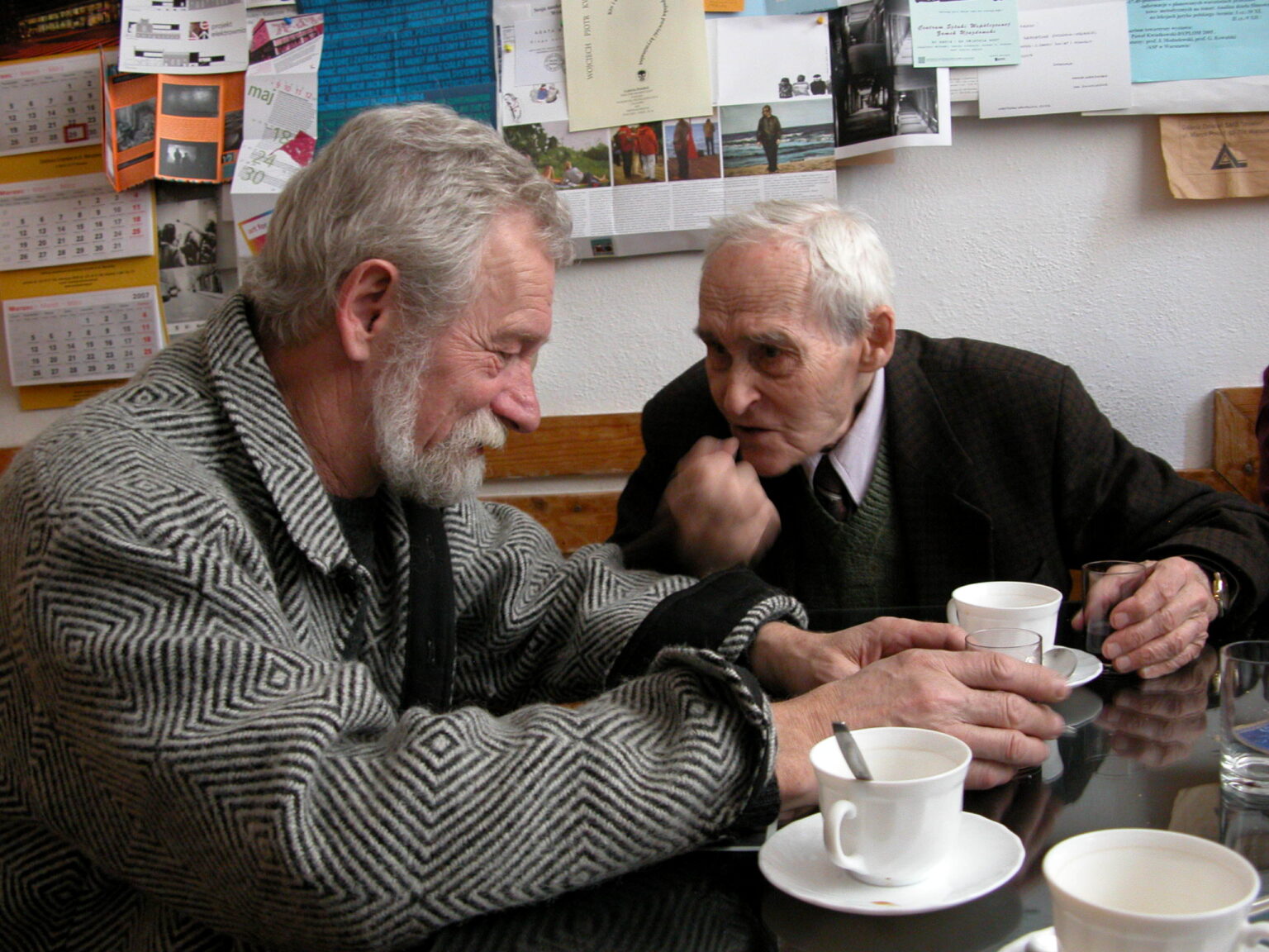 Kolorowe zdjęcie dwóch mężczyzn rozmawiających przy stole; na stole filiżanki