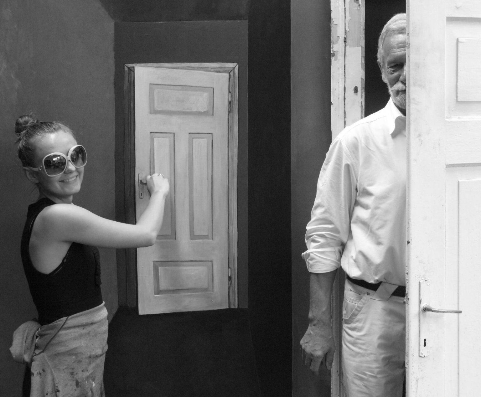 Czarno-białe zdjęcie. Na pierwszym planie mężczyzna ubrany na biało; na drugim kobieta w okularach przeciwsłonecznych