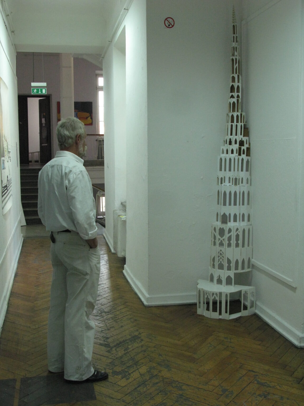 Mężczyzna w korytarzu; tyłem - przygląda się przestrzennej, pionowej pracy ustawionej w rogu