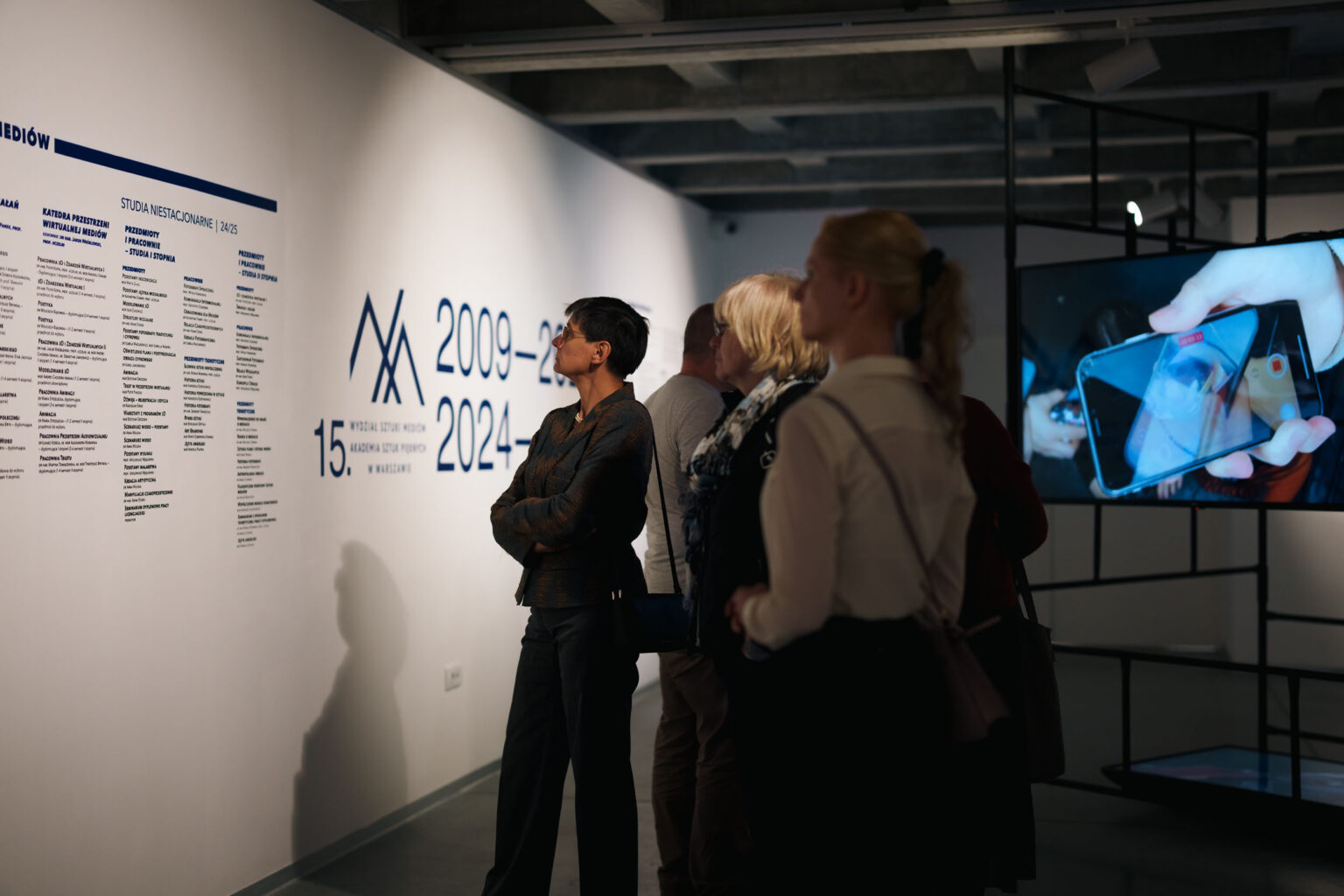 zwiedzający czytają o wystawie na ścianie galerii