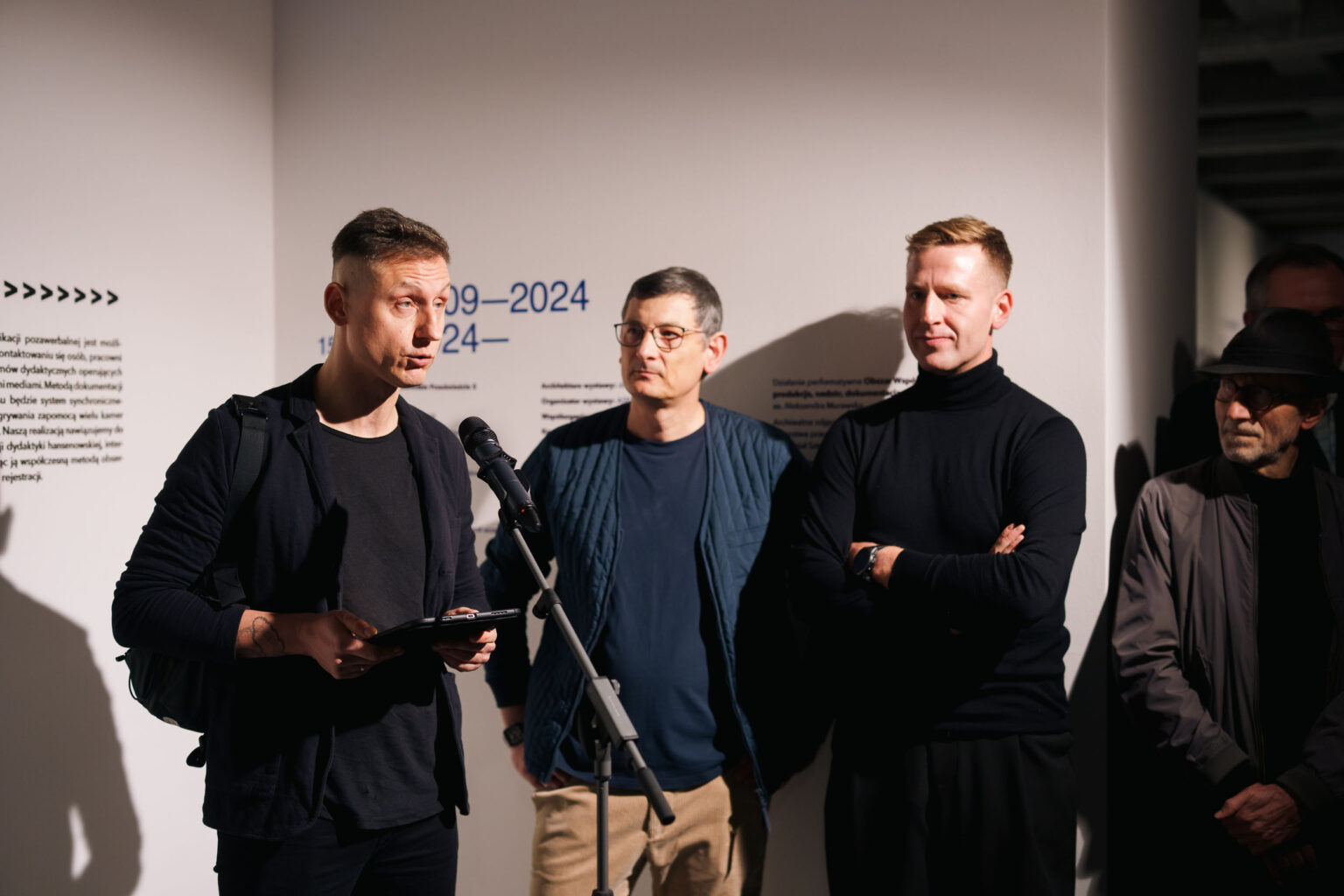 trzech mężczyzn, jeden mówi do mikrofonu