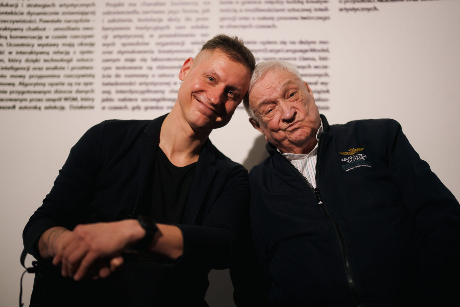 dwaj mężczyźnisiedzą obok siebie stykając się głowami