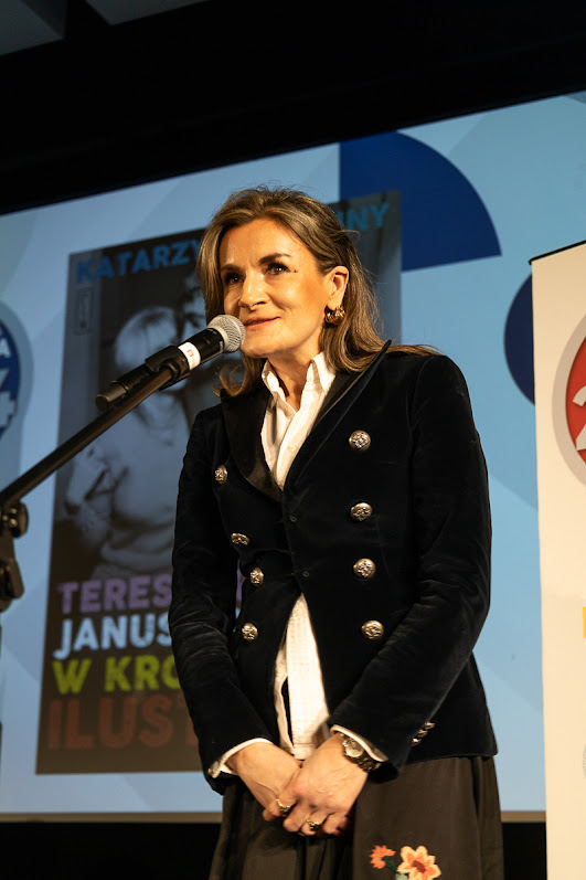 kobieta w żakiecie ze złotymi guzikami przy mikrofonie