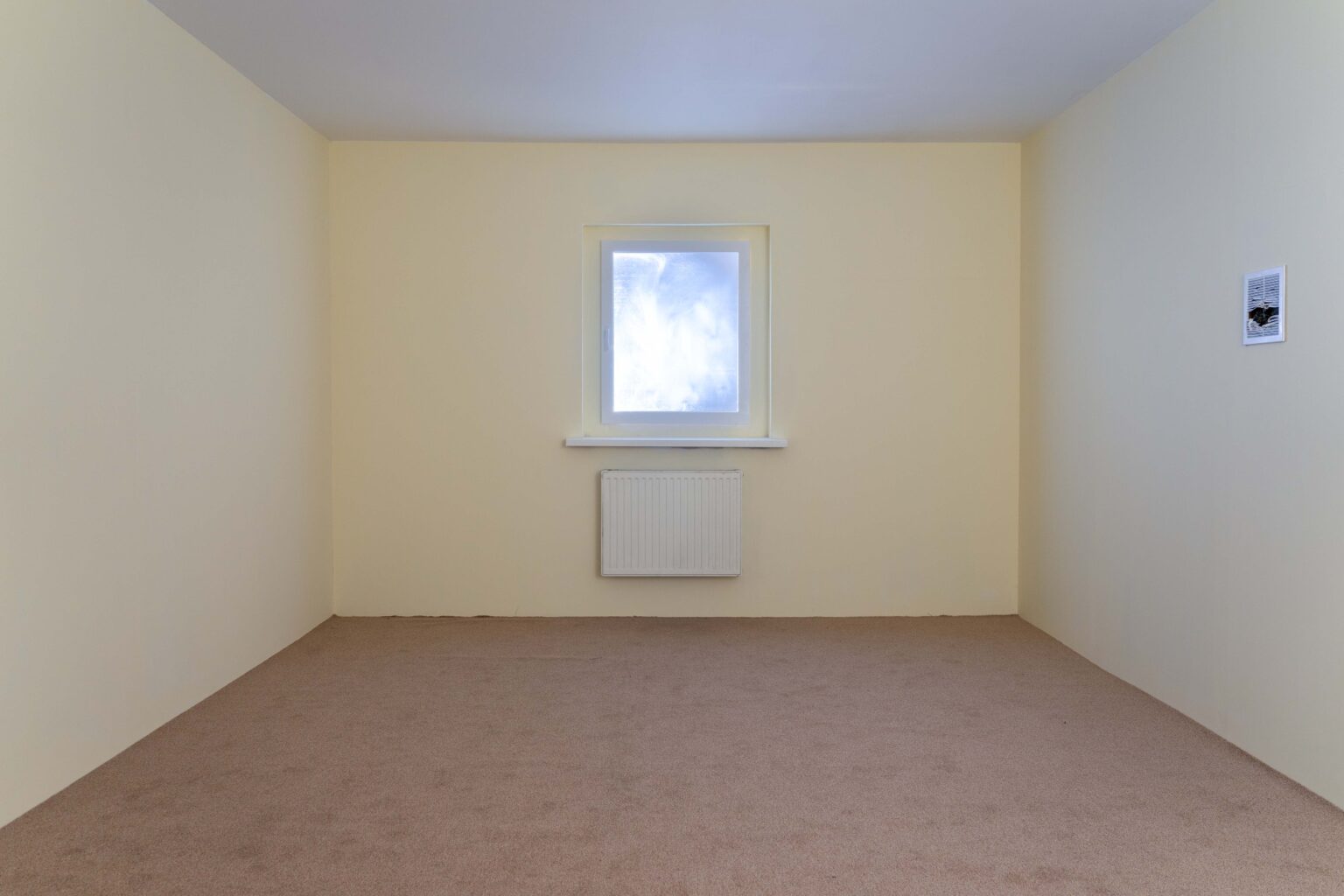 instalacja: widok 3 ścian pokoju z żółtymi ścianami, na wprost okno, kaloryfer, po prawej: dziurawy wywietrznik