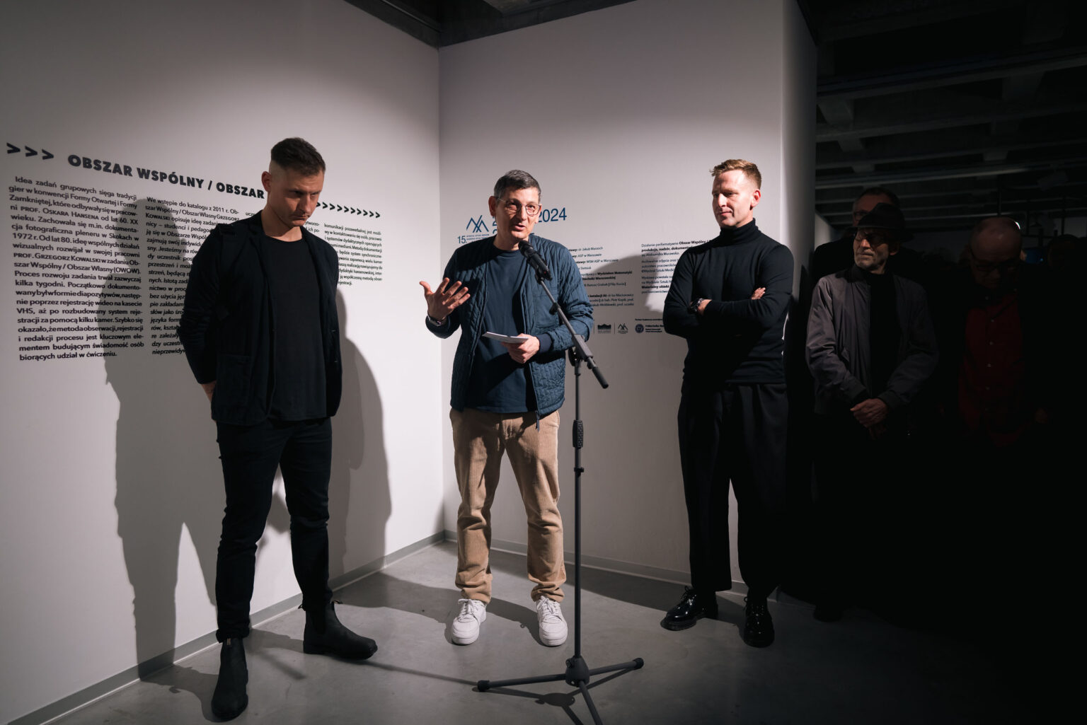 trzech mężczyzn, jeden z nich gestykuluje mówiąc do mikrofonu