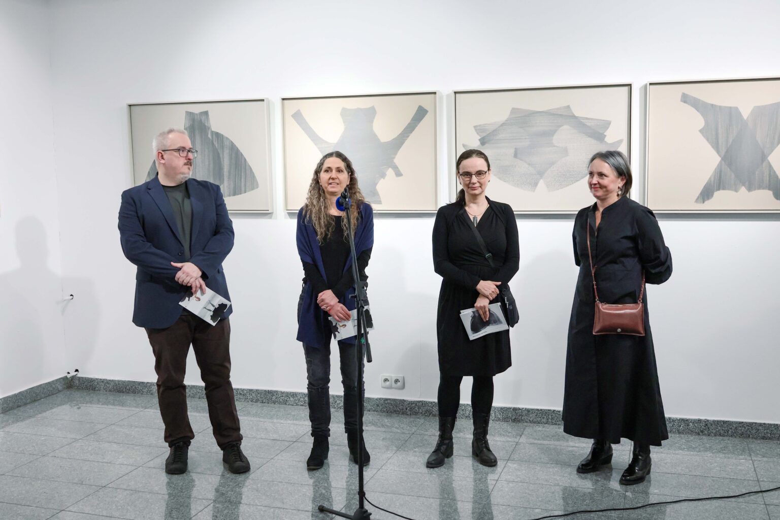 cztery osoby stoją w rzędzie, za nimi rysunki na ścianie galerii