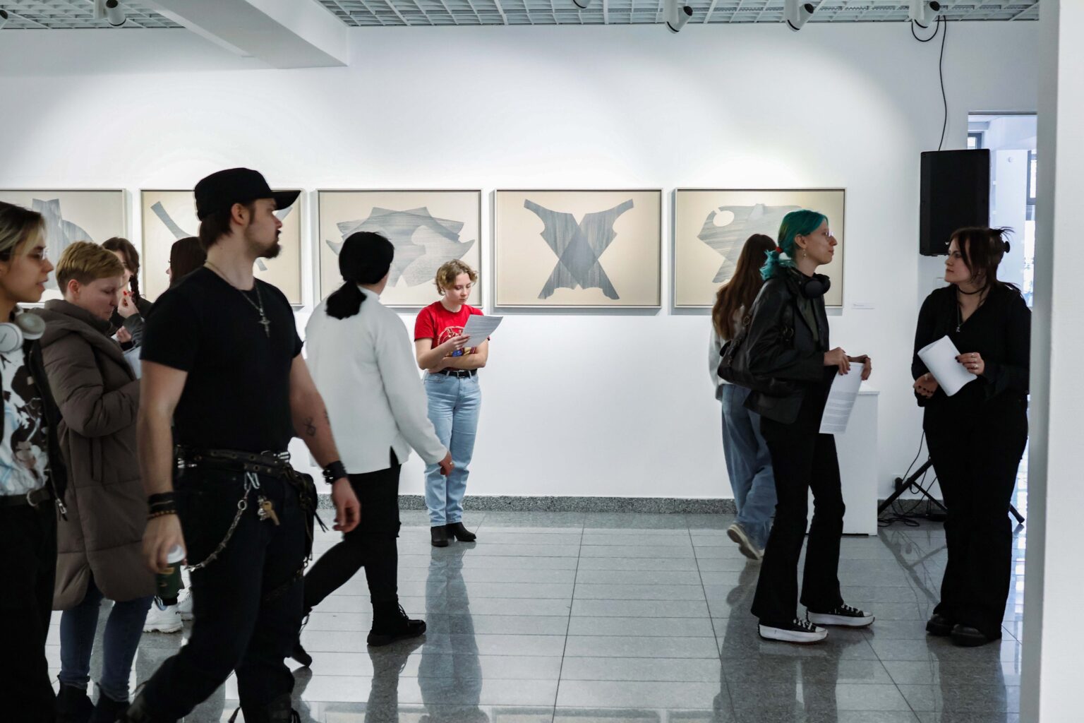 kilka osób zwiedających w przestrzeni galerii, rysunki na drugim planie