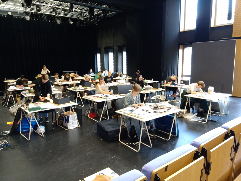 aula wykładowa z fioletowymi siedzeniami i białe stoliki