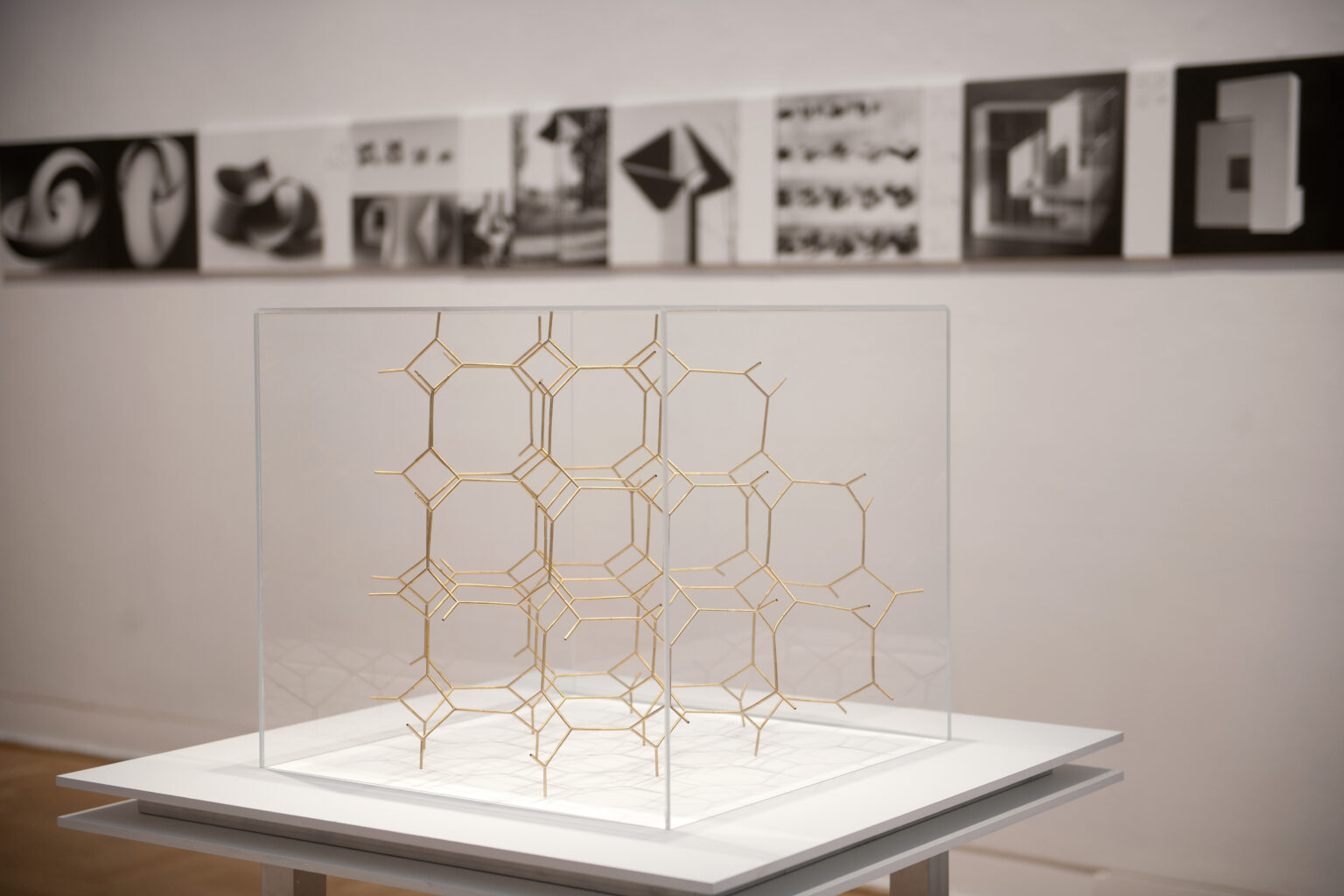 Przybliżenie na geometryczną siatkę, wykonaną z drutu w złotym kolorze. Siatka znajduje się w gablocie.