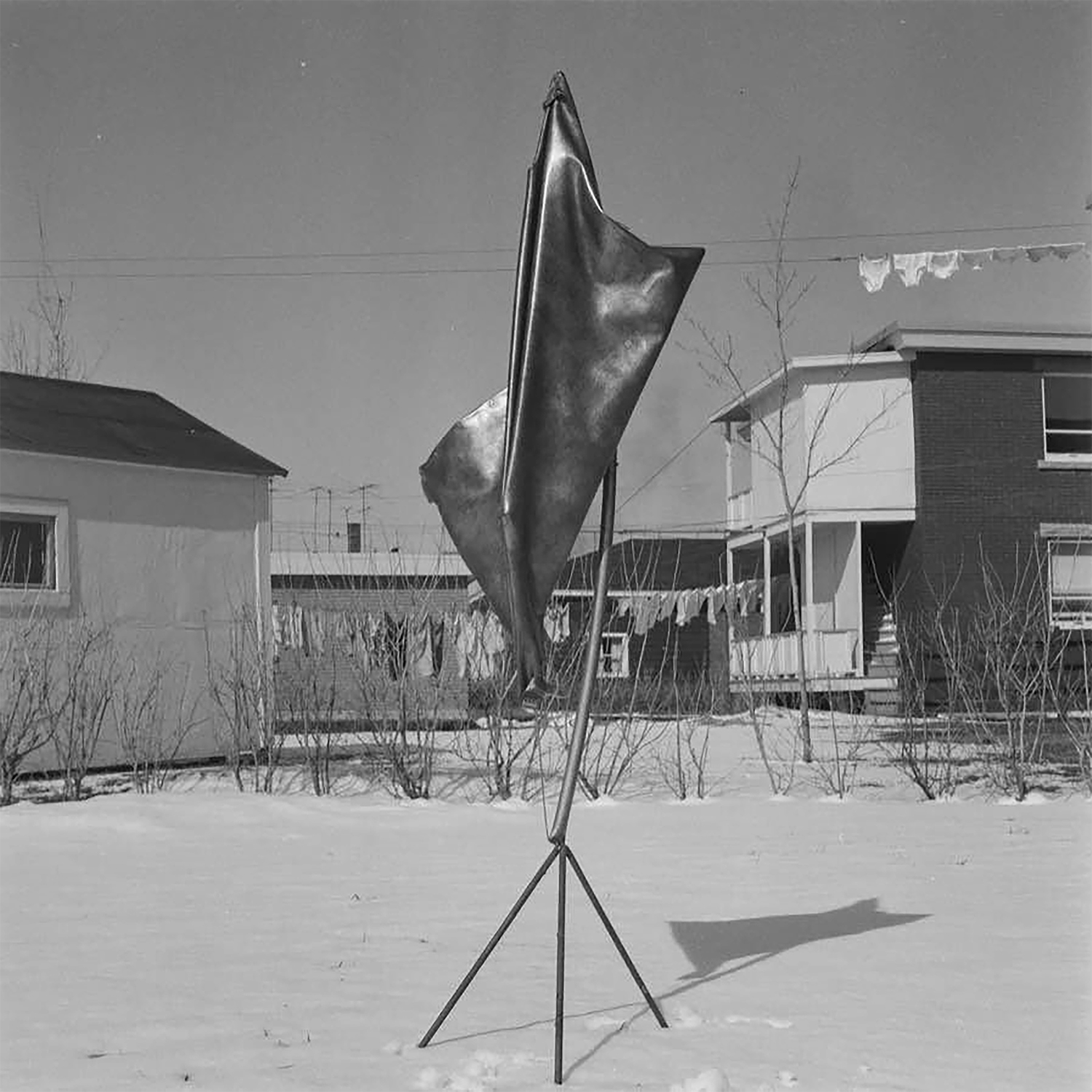 czarno-białe zdjęcie obiektu z metalu, w tle budynki i pranie na sznurku