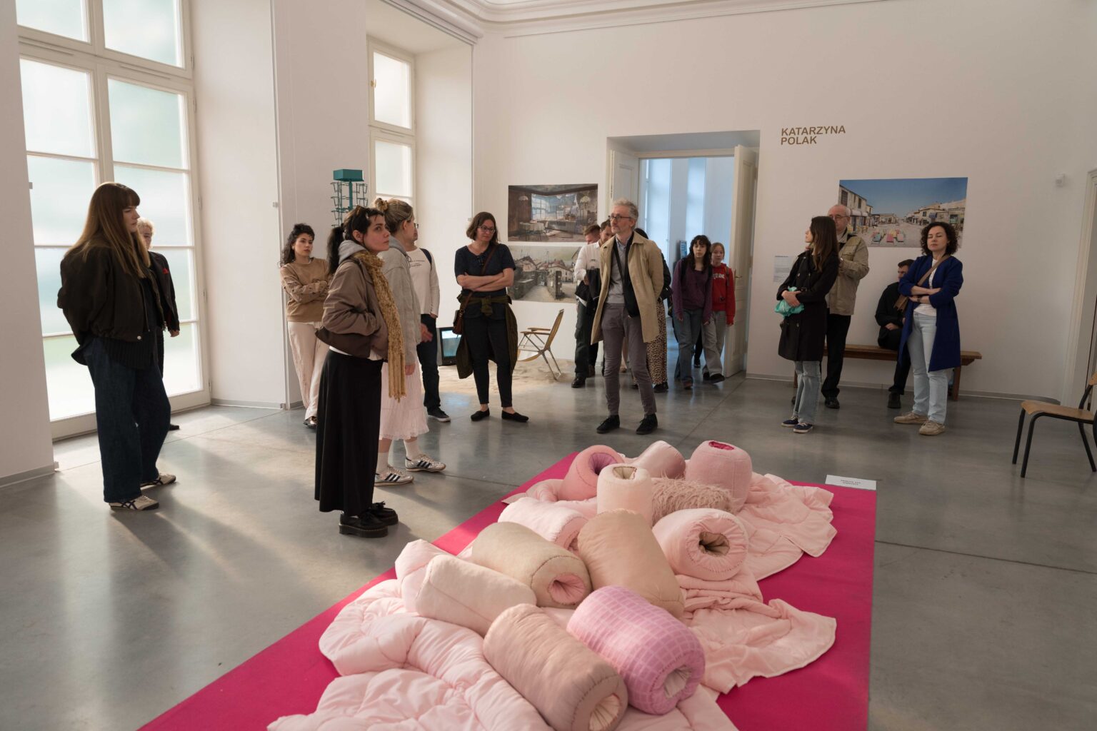 grupa ludzi na wystawie, po środku, na podłodze sterta różowych poduszek
