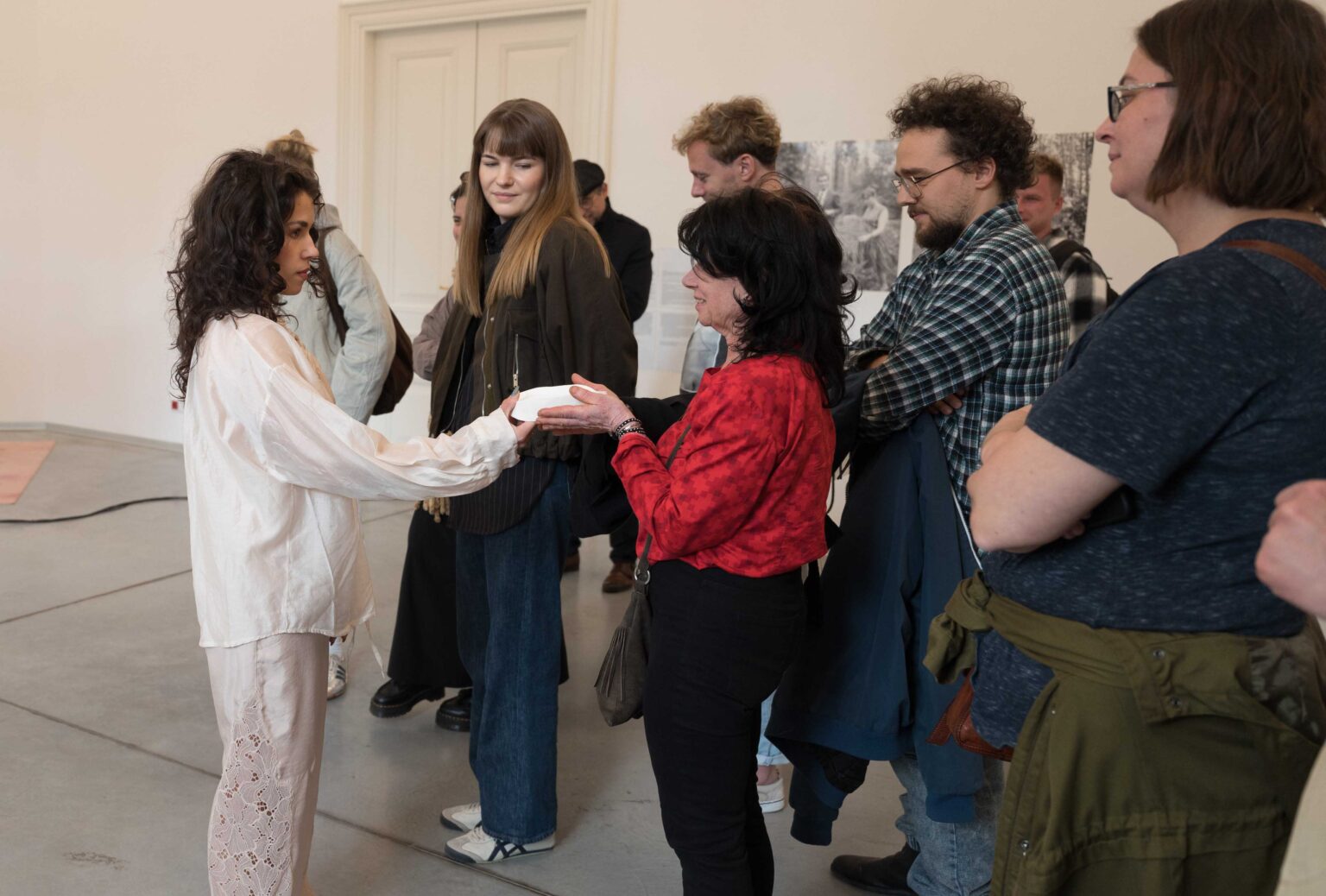 grupa osób, kobieta w białym stroju podaje im białe naczynie