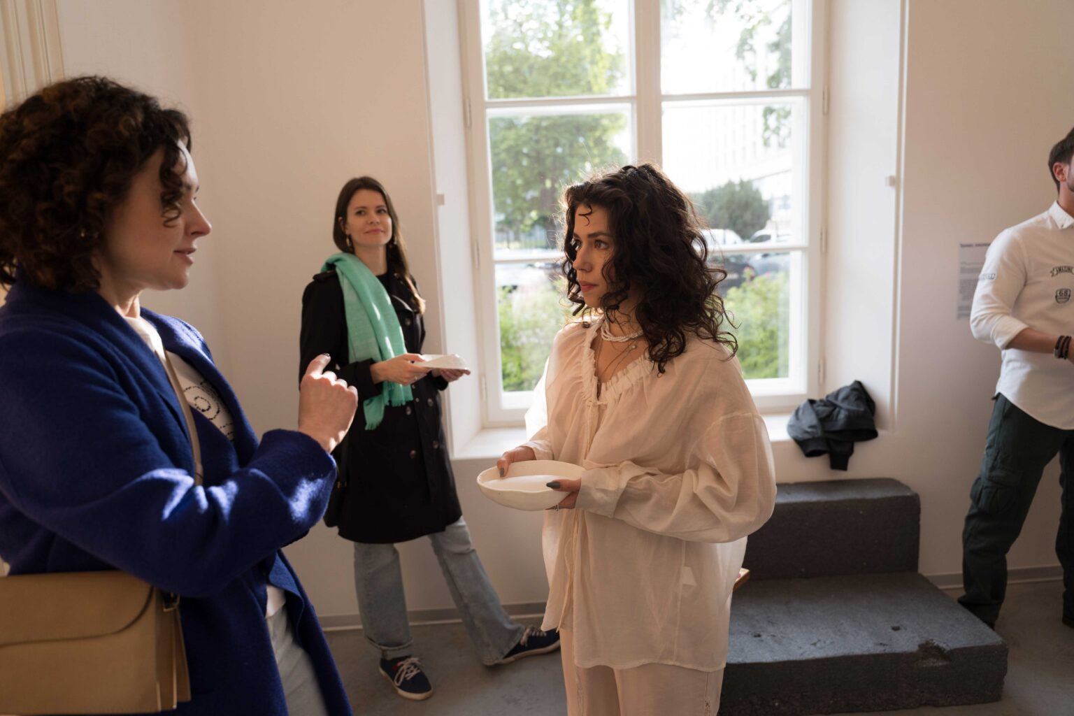 grupa osób, kobieta w białym stroju podaje im białe naczynie