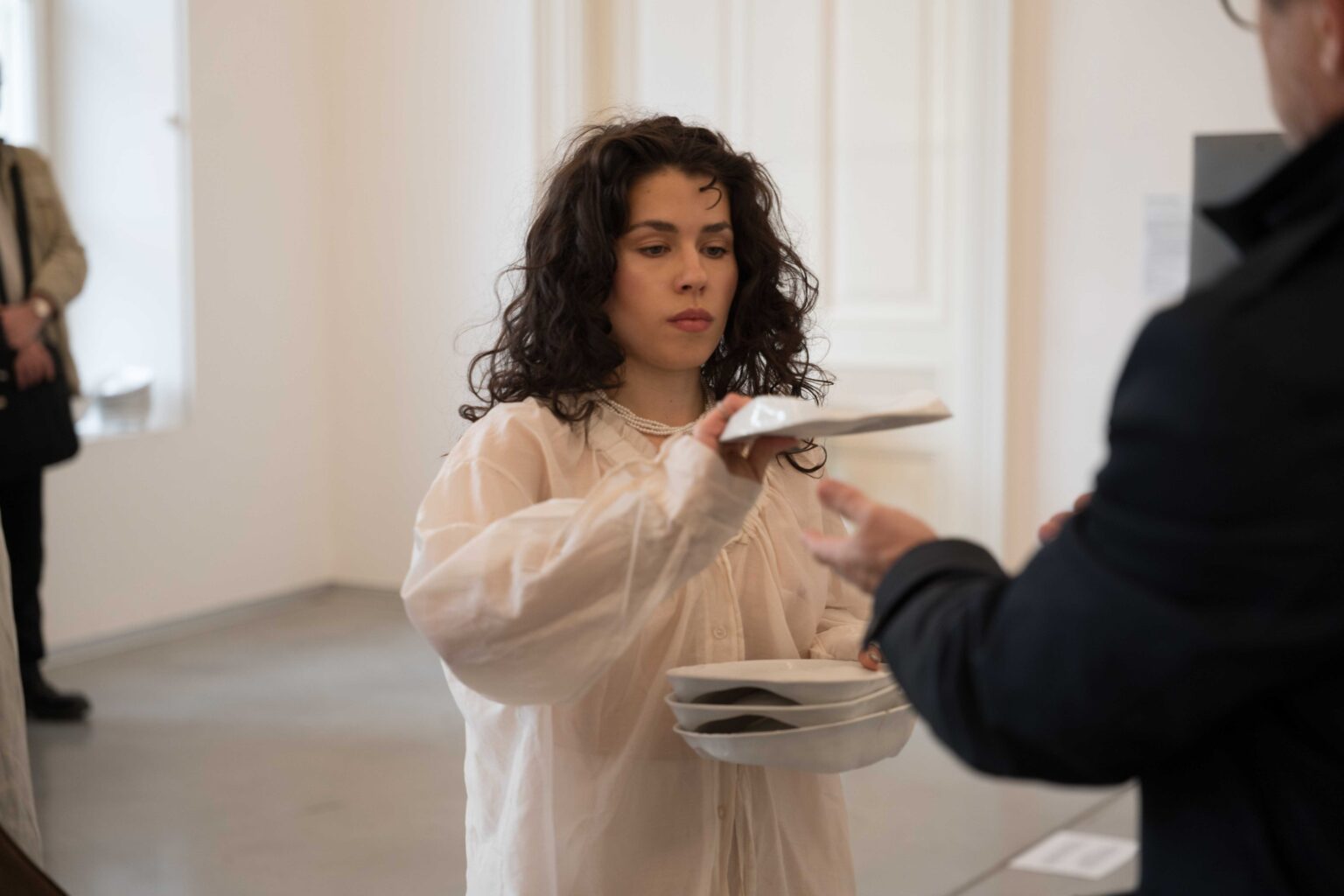 grupa osób, kobieta w białym stroju podaje im białe naczynie