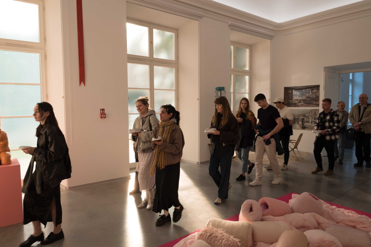 grupa osób z naczyniami w rękach przechodzi przez galerię