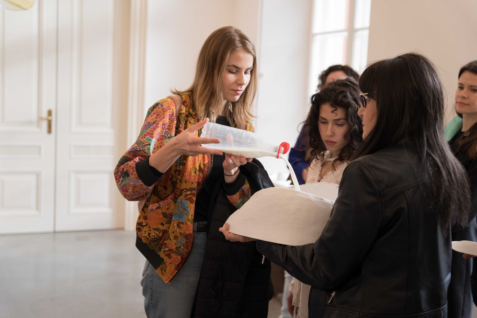 kobieta nalewa mleko do dużego, białego naczynie trzymanego przez inne osoby