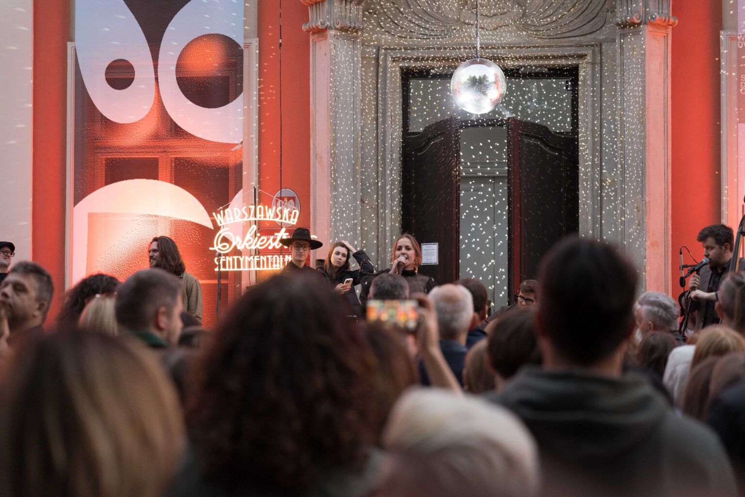 zespół na scenie, w tle czerwony budynek, nad wejściem do niego wisi dyskotekowa kula