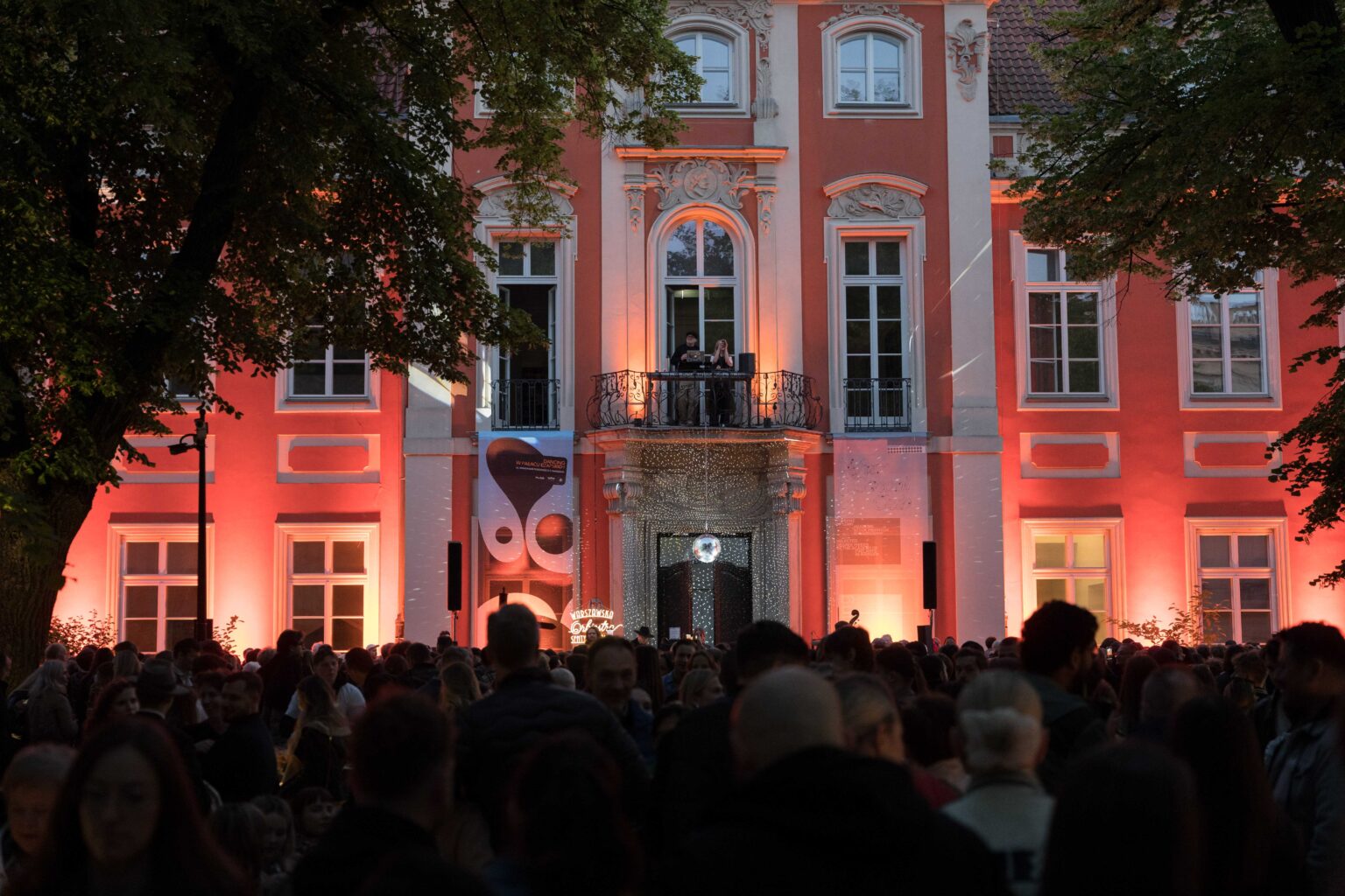 tłum ludzi przed podświetlonym na czerwono pałacem