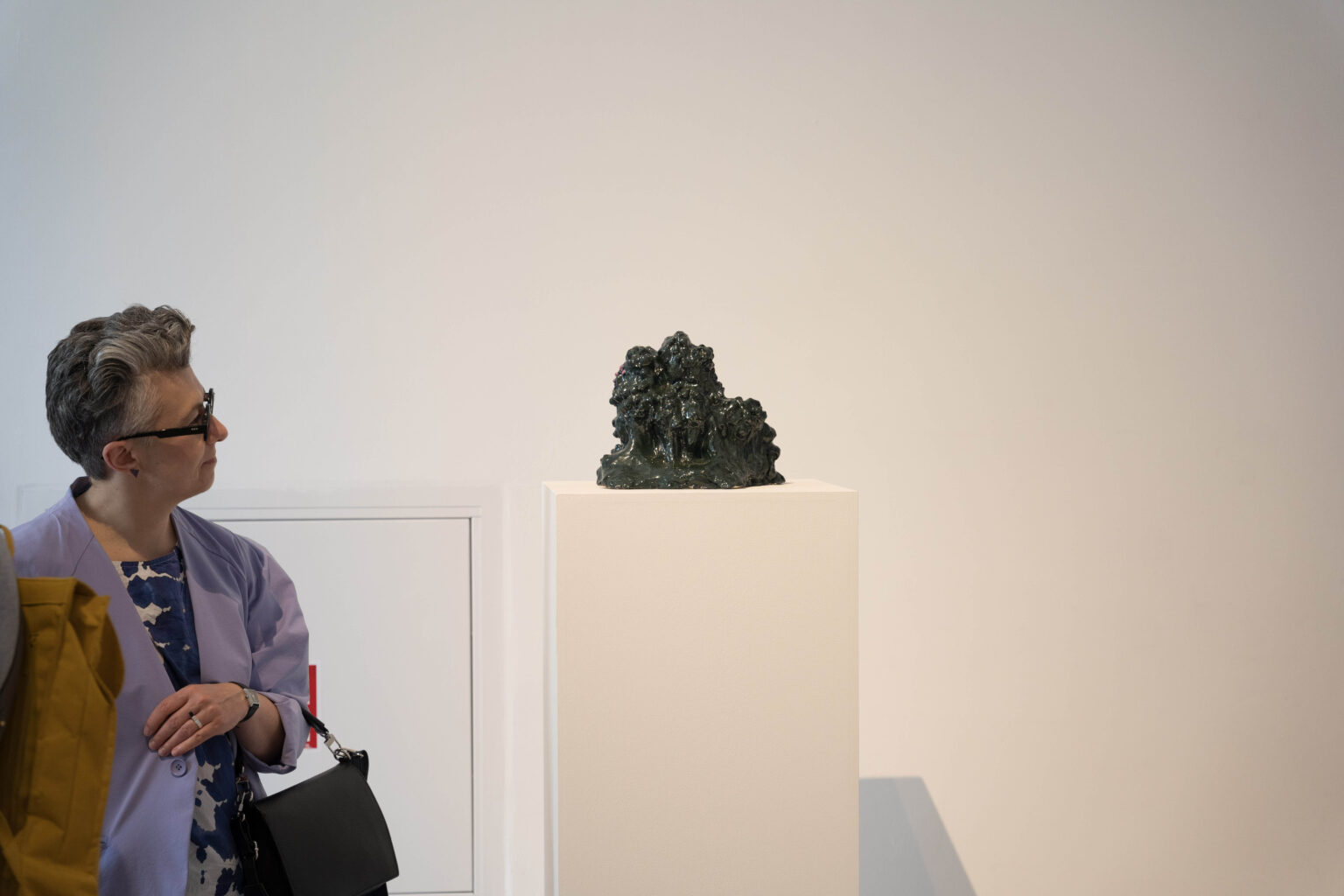 czarna rzeźba na białym postumencie i osoba oglądająca ją