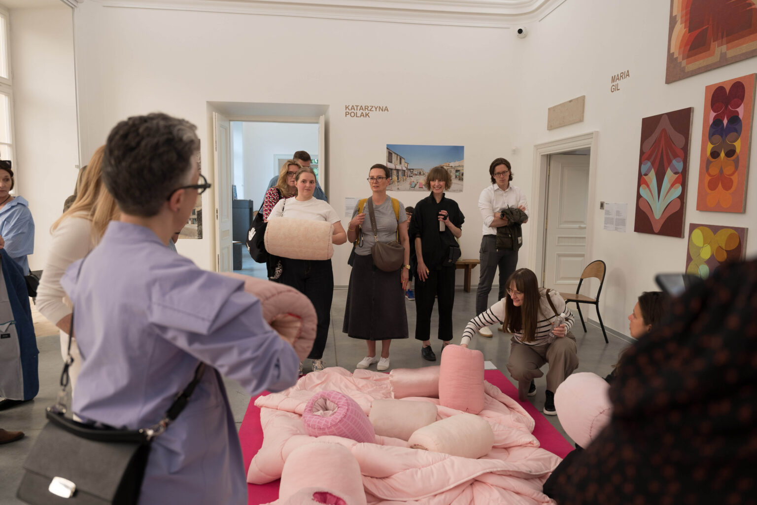 różowe miękkie obiekty przypominjące poduch na podłodze w przestrzeni wystawy, wokół grupa ludzi