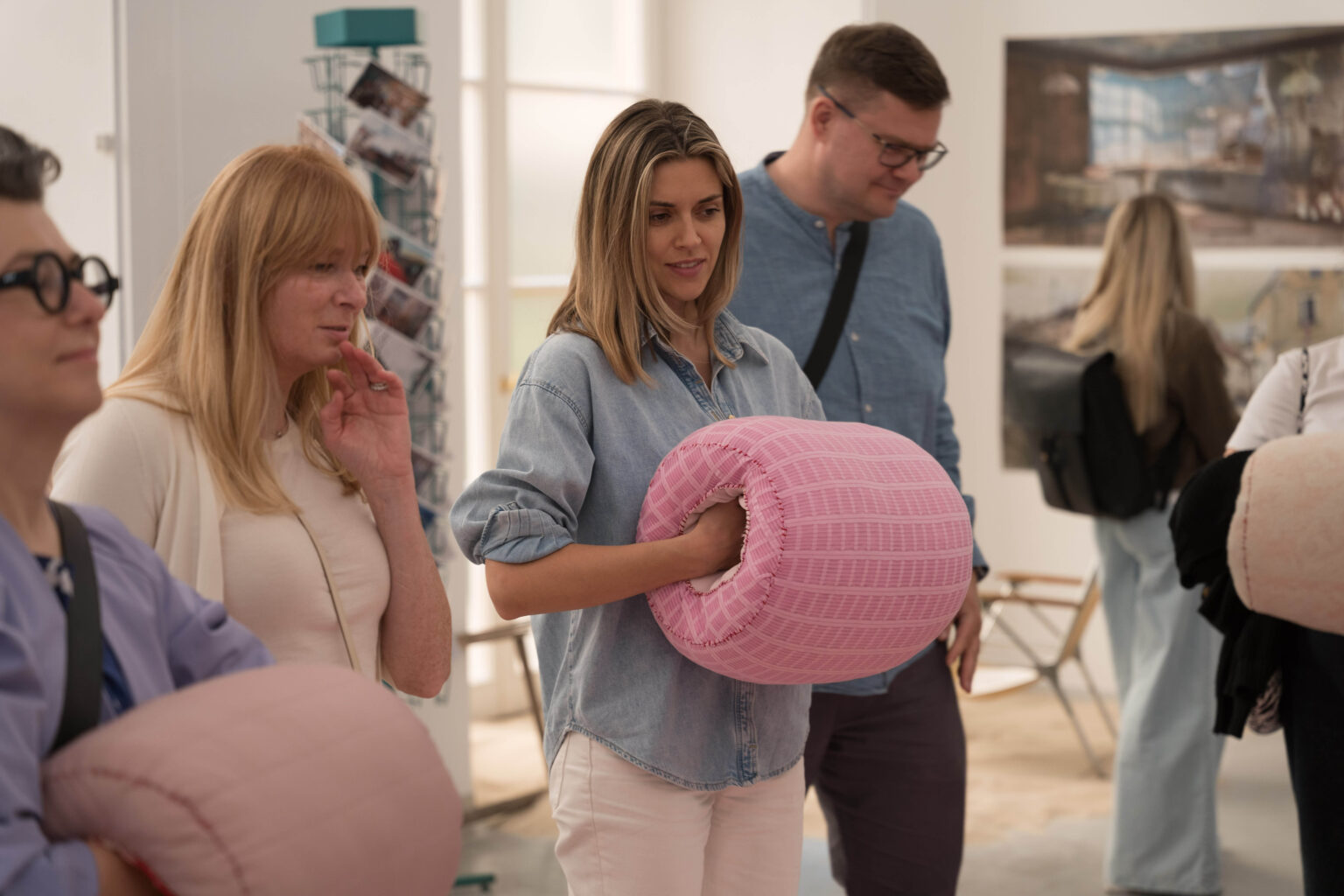 trzy osoby, kobieta w środku trzyma w dłoniach okrągły, miękki, różowy przedmiot