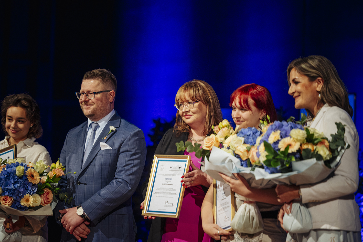 kilka osób z kwiatami i dyplomami